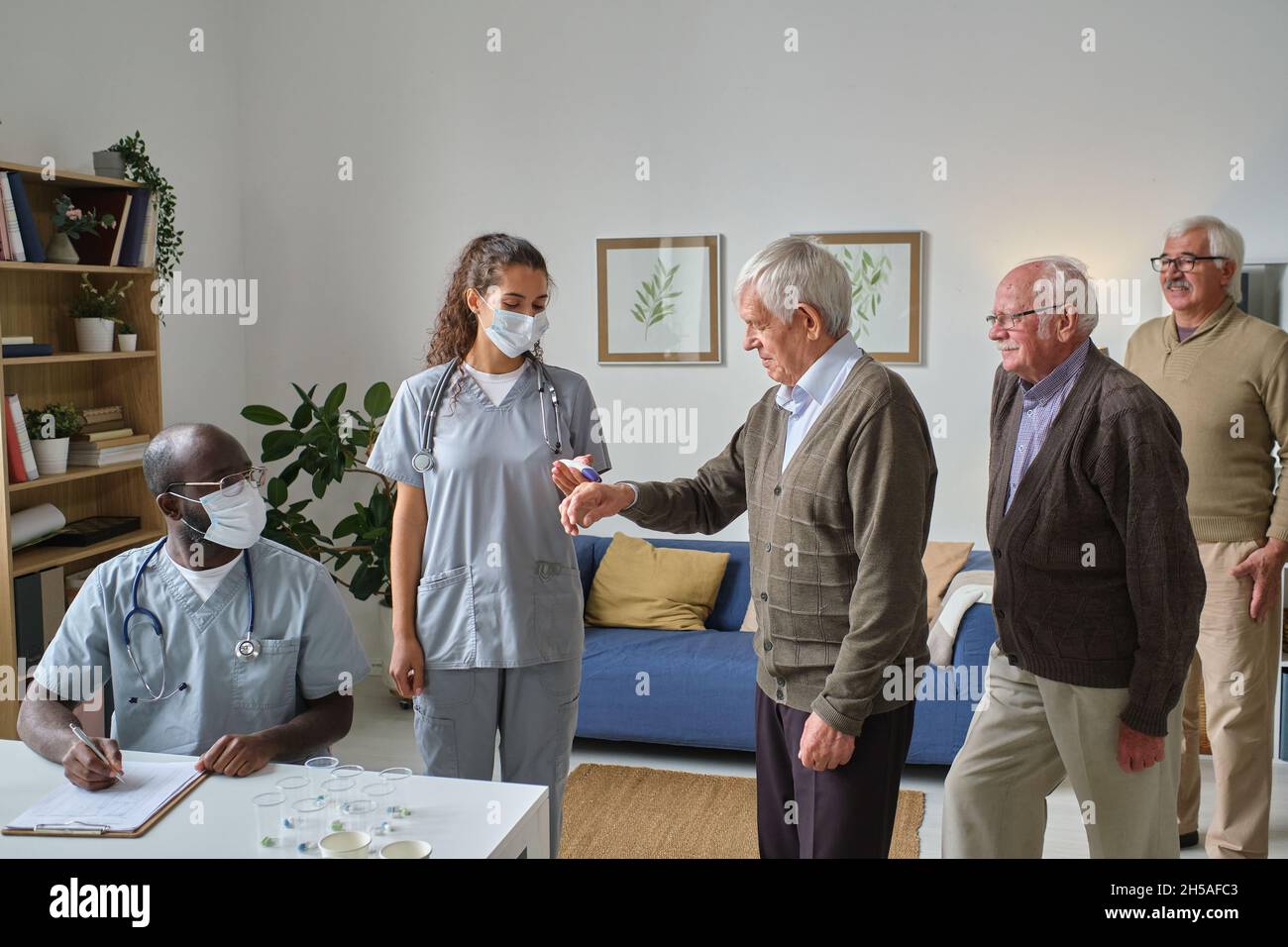 Zwei Ärzte, die Bluttests durchführen und ältere Menschen untersuchen, während sie in einer Reihe im Raum stehen Stockfoto