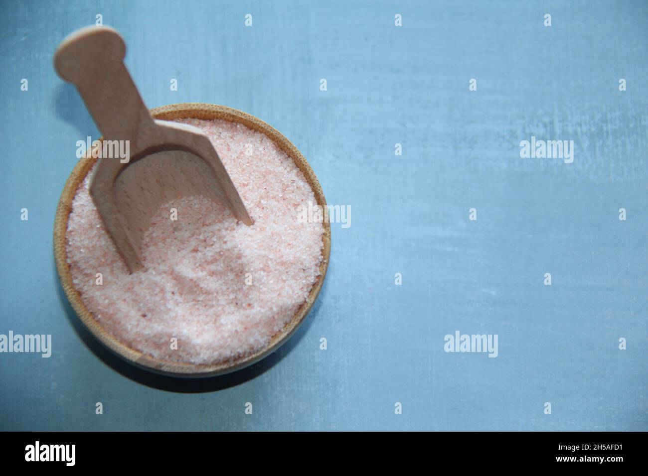 Himalaya-Salz, rosa, in einer Holzschale, mit einem hölzernen Messlöffel auf einem antiken Holztisch. Blick von oben. Stockfoto