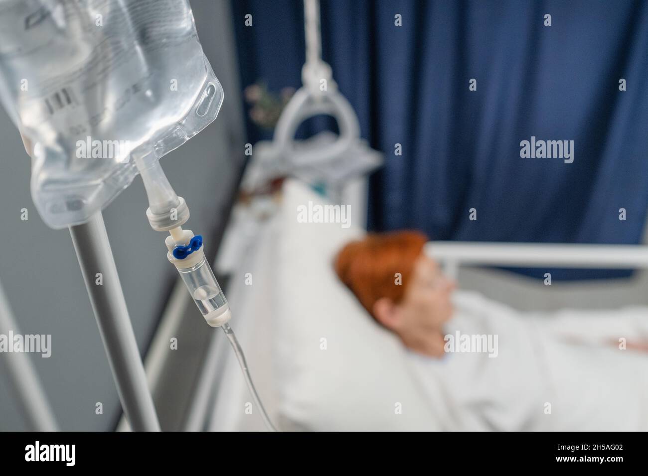 Nahaufnahme eines infusionstropfes, der über dem Bett hängt, mit dem Patienten auf der Krankenhausstation Stockfoto