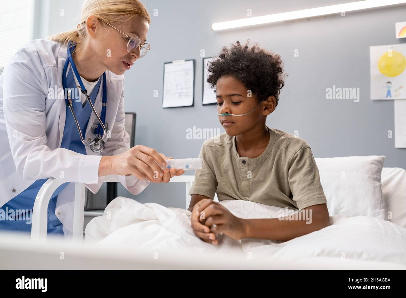 Ärztin, die IV-Tropf für einen kleinen Jungen macht, der während seiner Behandlung im Krankenhaus auf dem Bett sitzt Stockfoto