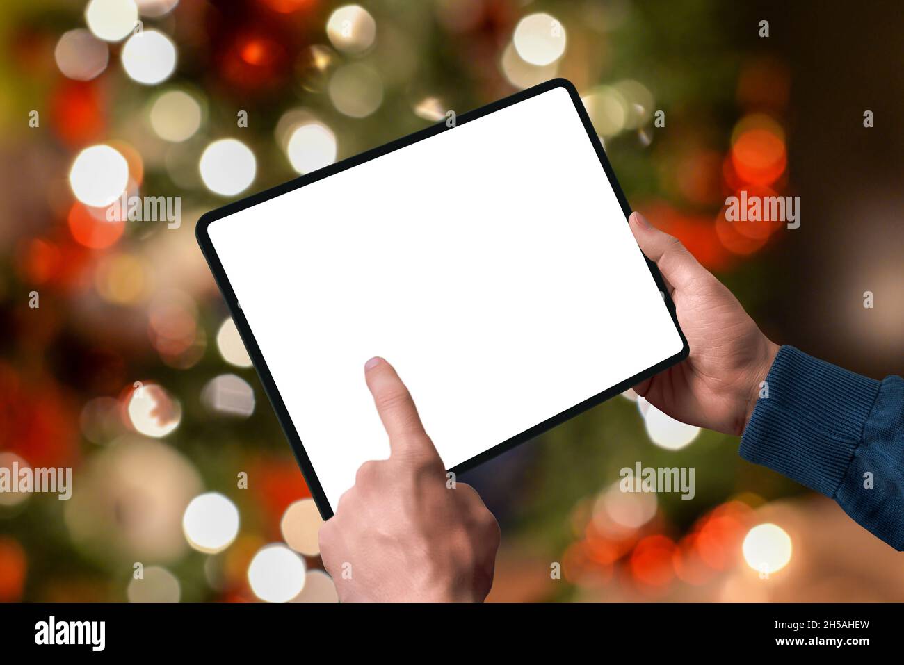 Tablet in den Händen mit den Lichtern des Weihnachtsbaums dahinter. Isoliertes Display zur Designförderung. Online-Shopping-Konzept der Saison Stockfoto