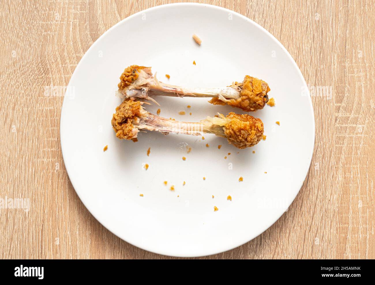 Zwei Hühnerknochen, die auf einem weißen Teller übrig sind. Ungesunde Fast Food, Hühnerbeine, Draufsicht Stockfoto