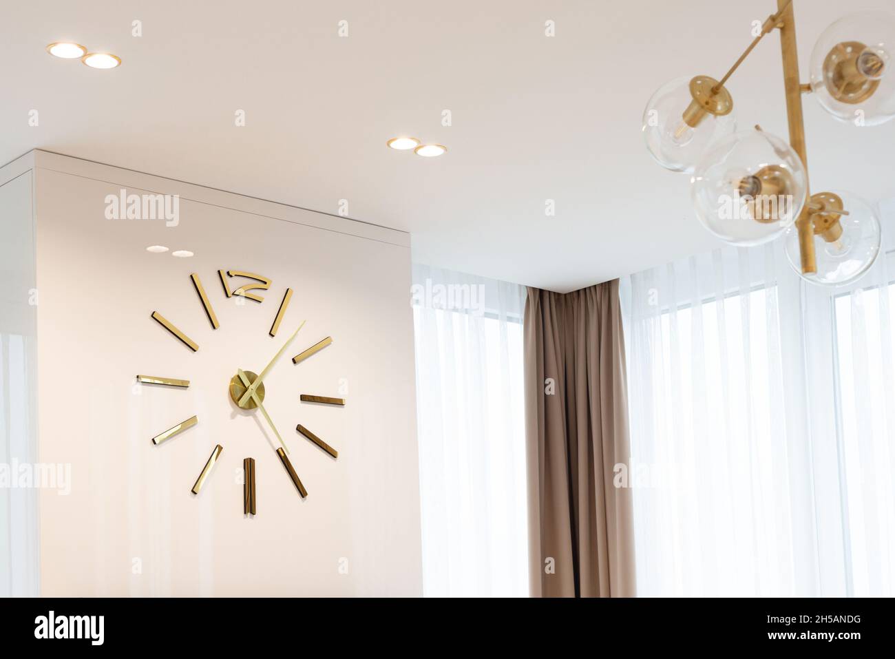 Eine riesige Uhr in Goldfarbe an der Wand in einem modernen beigefarbenen Interieur. Innenarchitektur. Weicher, selektiver Fokus, künstlerisches Rauschen. Stockfoto