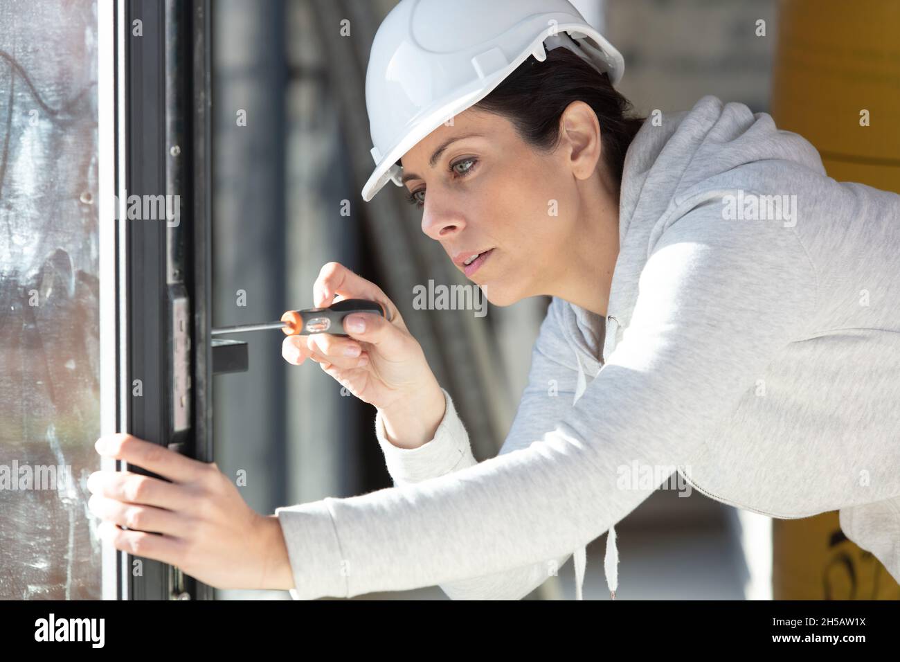 Junge Frau entschrauben einen Fenstergriff mit einem Schraubendreher Stockfoto