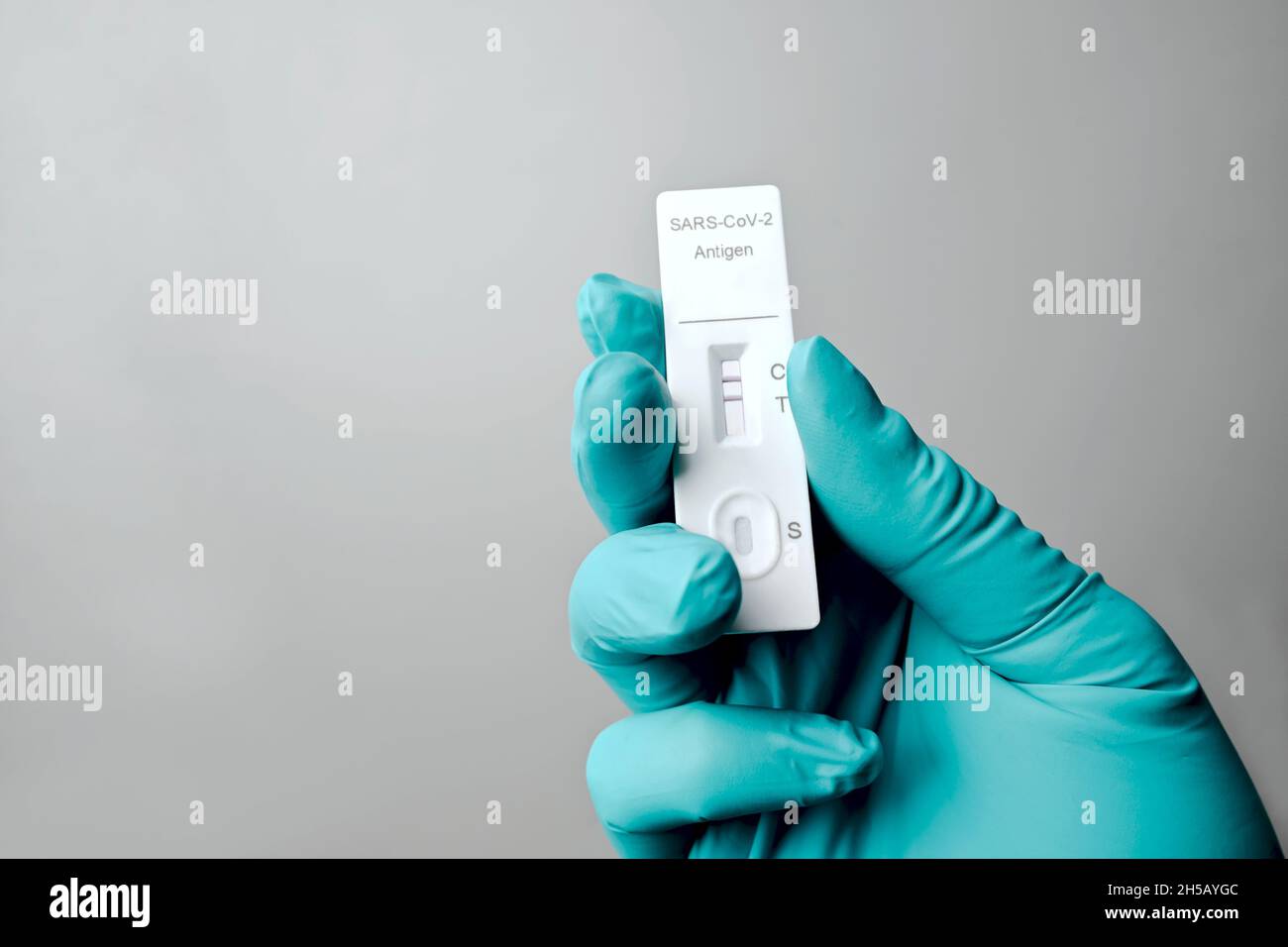 Handschuhen mit positivem Schnelltestgerät für COVID-19. Isoliert auf grauem Hintergrund. Stockfoto