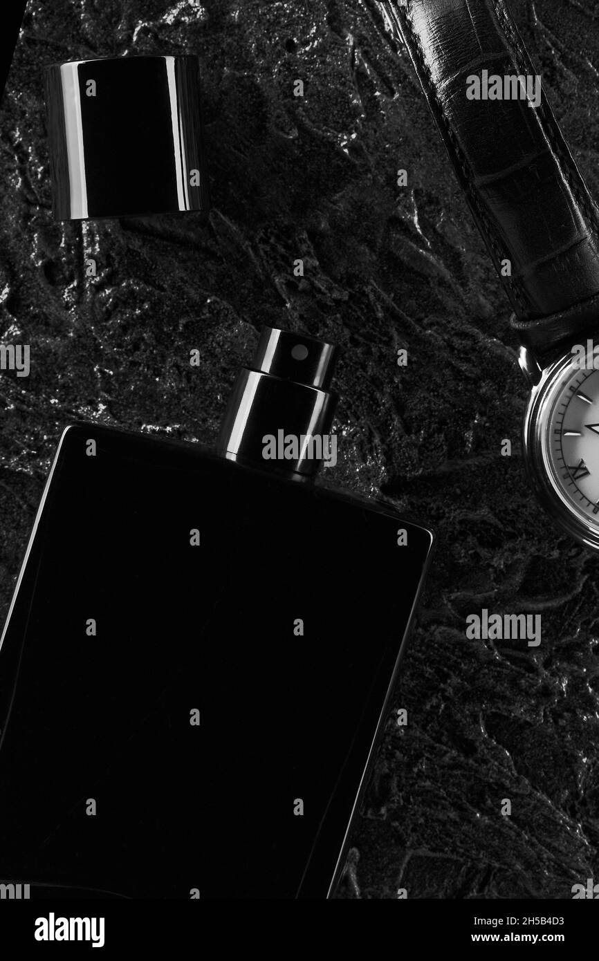 Herrenuhren und eine offene Flasche schwarzes Eau de Toilette liegen auf einem dunklen strukturierten Hintergrund. Duft für Männer. Flaches Lay Stockfoto