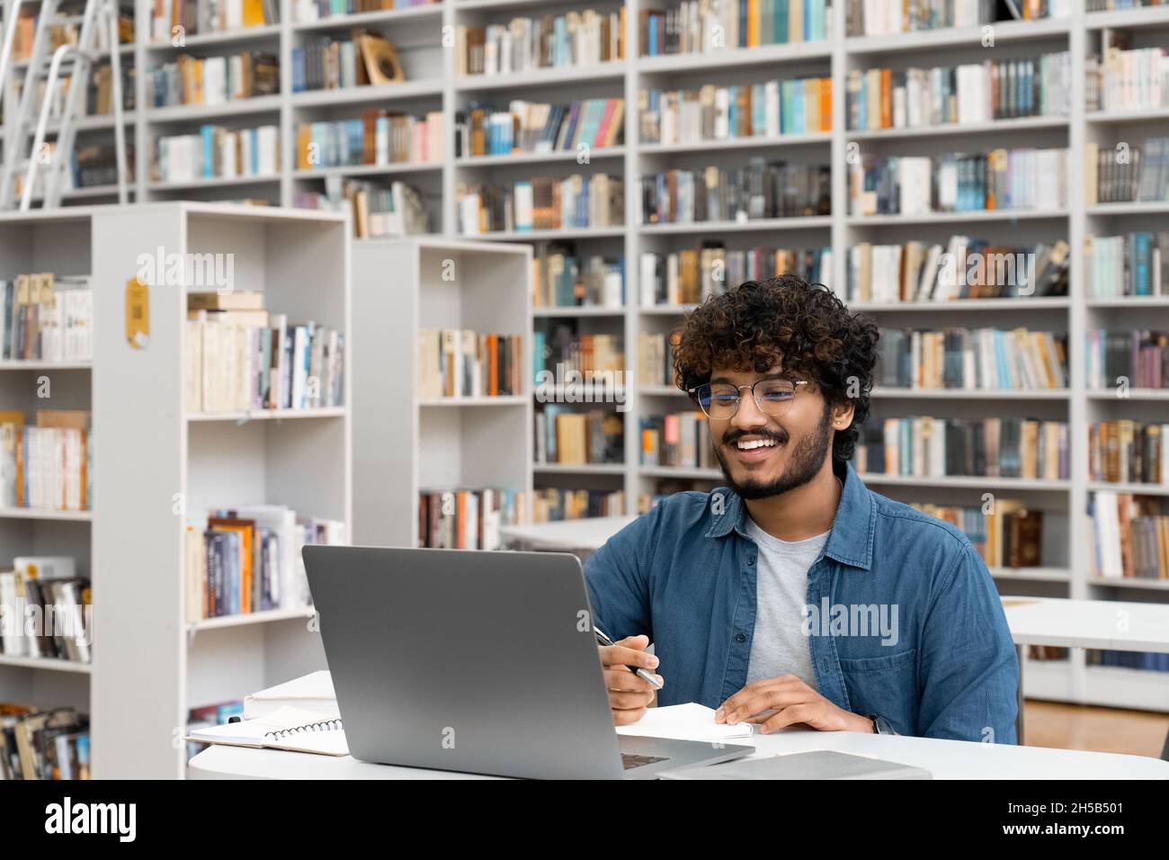 Männlicher Student, der in der Universitätsbibliothek mit einem Laptop studiert und Videoanruf führt Stockfoto