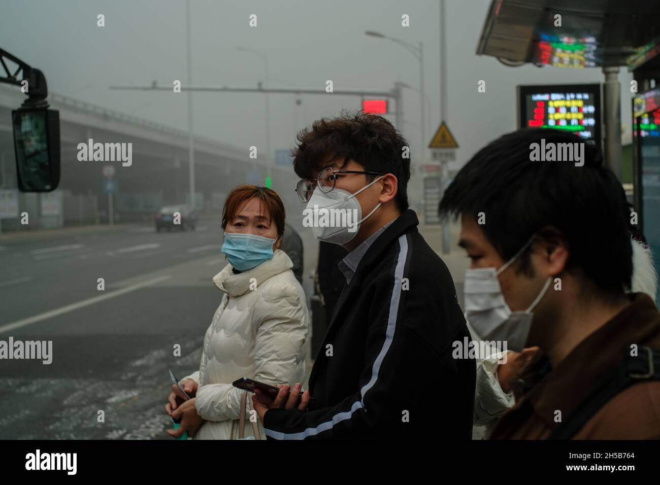 An einer Bushaltestelle in Peking, China, tragen Menschen Masken zum Schutz vor Covid-19 und schwerem Smog. 06-Nov-2021 Stockfoto