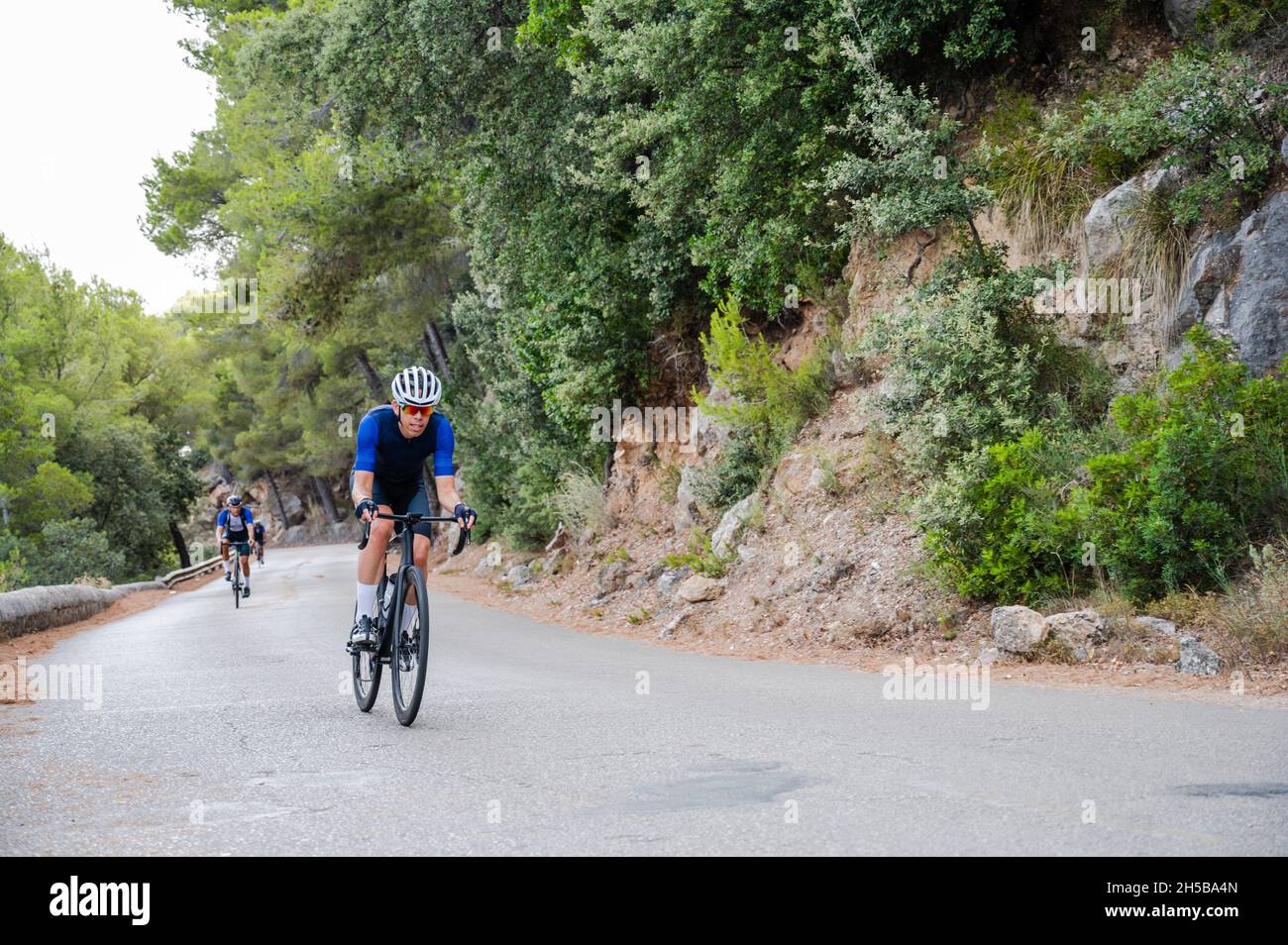 Radfahrer im Vordergrund auf einer Bergstraße mit einem anderen nicht erkennbaren Radfahrer im Hintergrund Stockfoto