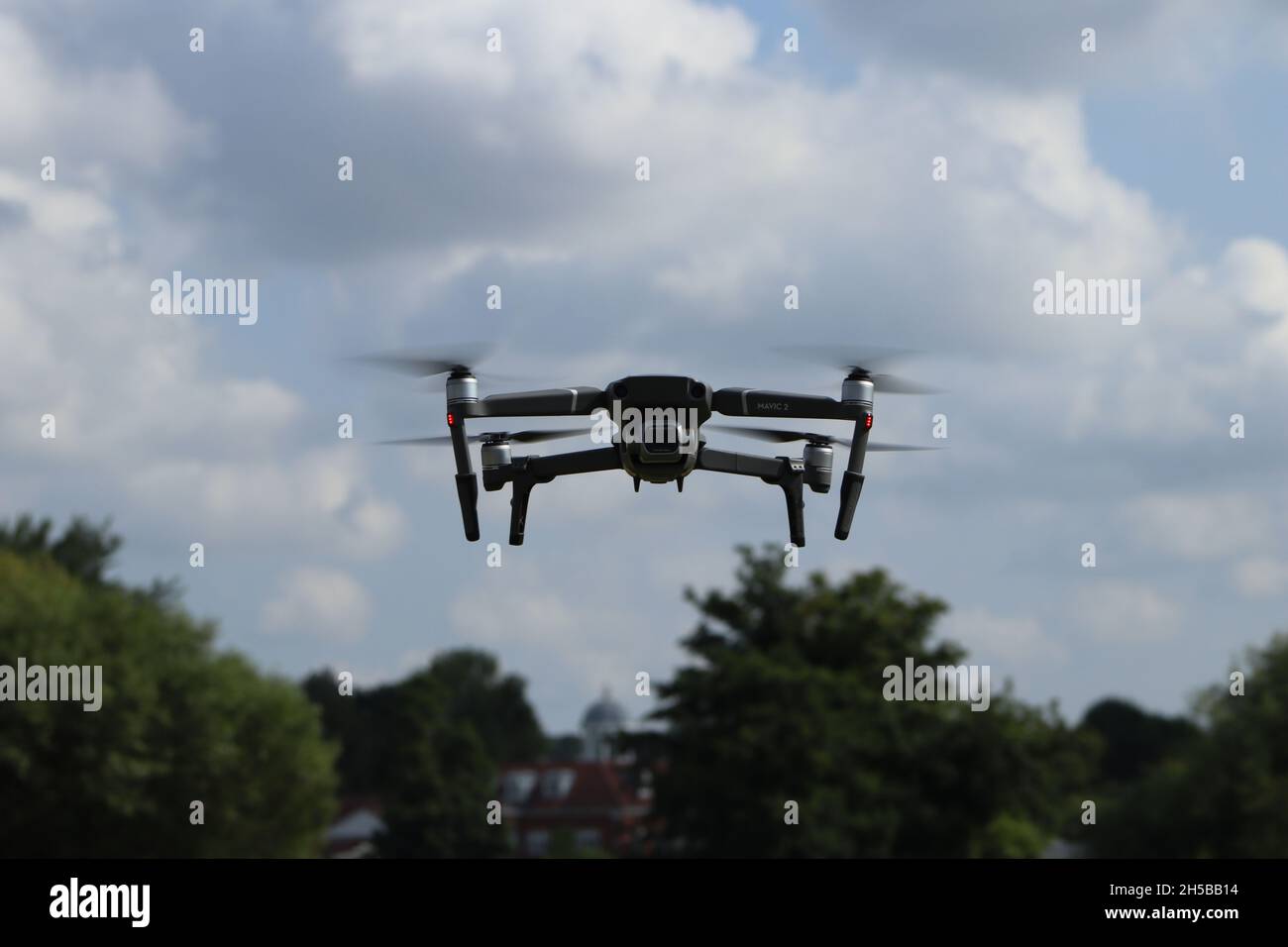 Eine DJI Mavic 2 Pro Drohne schwingt tagsüber in der Luft, mit blauem Himmel und einer hellen Wolkenkulisse. Die Drohne wird im Flug über einem belaubten A gefangen genommen Stockfoto