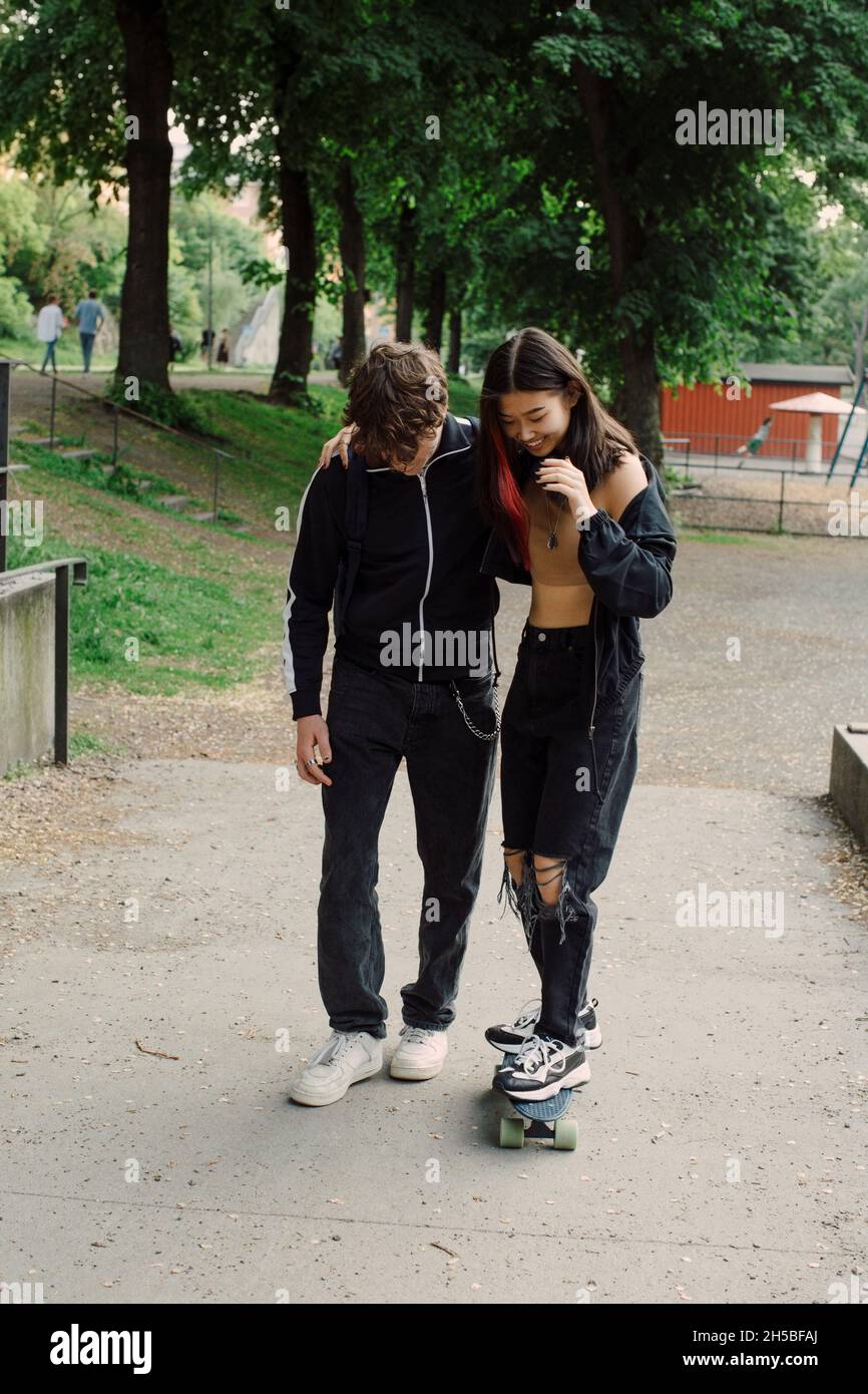 Teenager-Junge unterrichtet Skateboarding an Freundin im Park Stockfoto