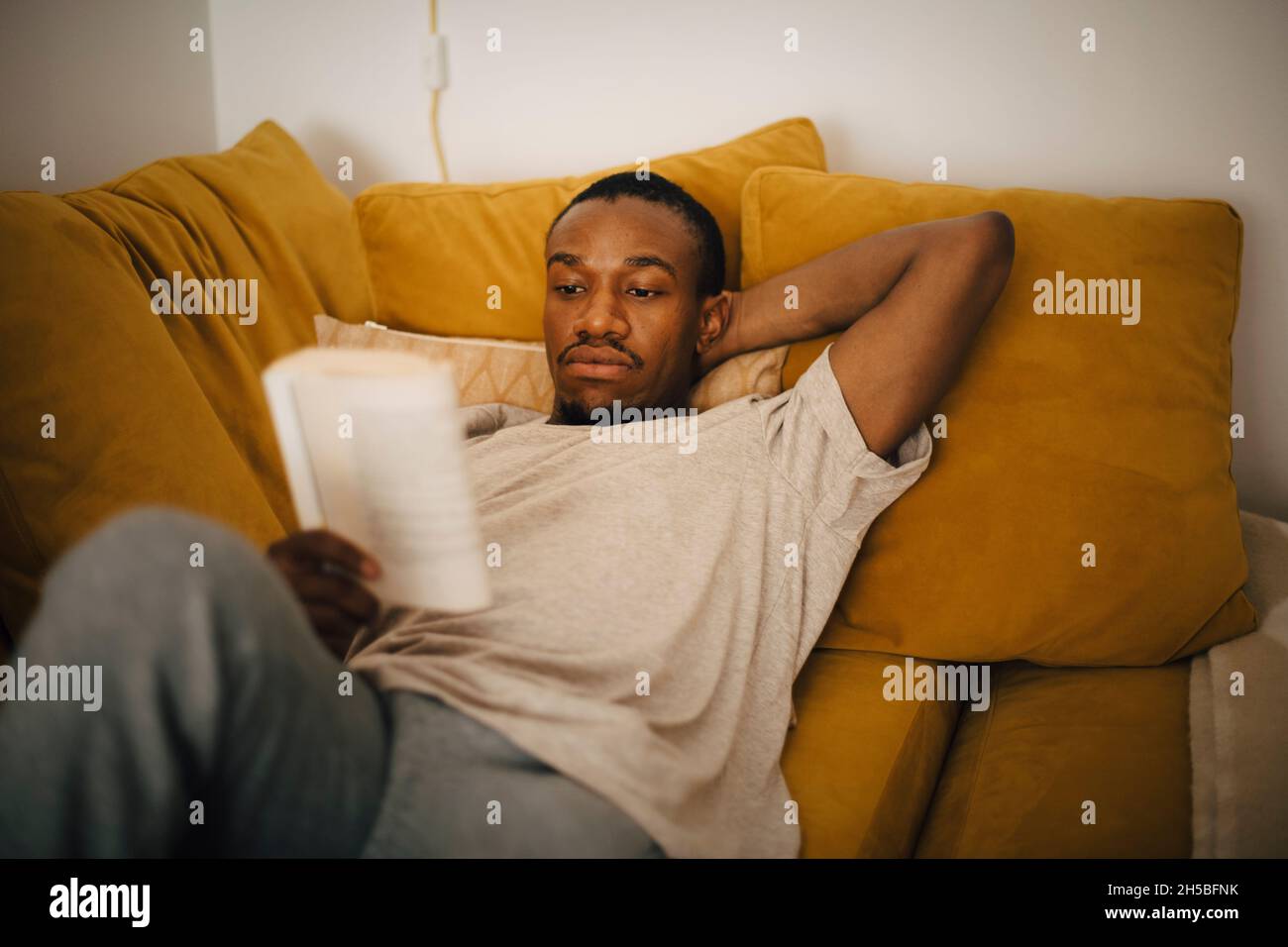 Ein Mann mittleren Erwachsenen liest ein Buch, während er zu Hause auf dem Sofa liegt Stockfoto Ein Mann mittleren Erwachsenen liest ein Buch, während er zu Hause auf dem Sofa liegt Stockfoto