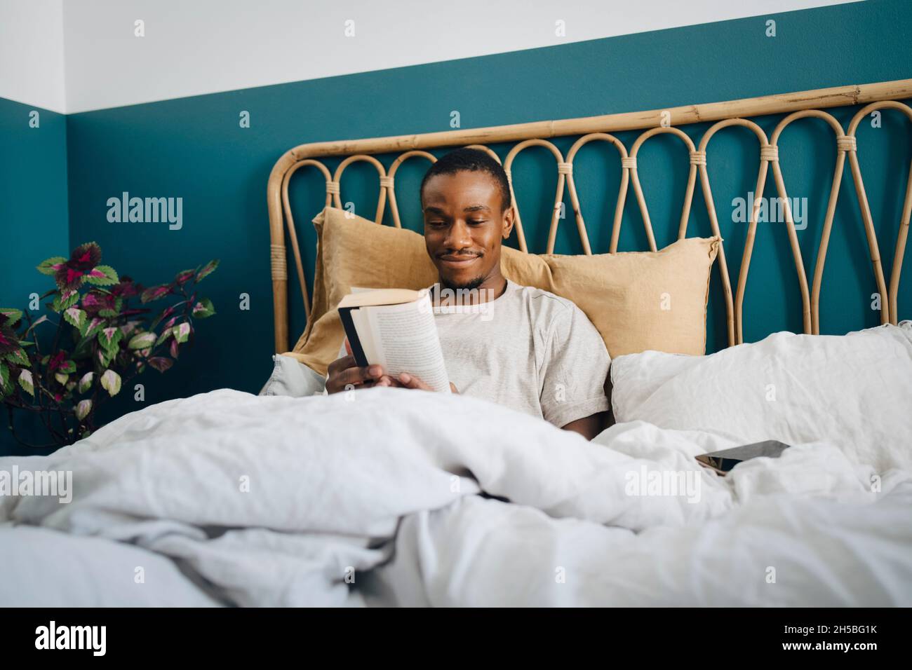 Lächelnder Mann mit mittlerem Erwachsenenalter, der zu Hause im Bett ein Buch liest Stockfoto Lächelnder Mann mit mittlerem Erwachsenenalter, der zu Hause im Bett ein Buch liest Stockfoto