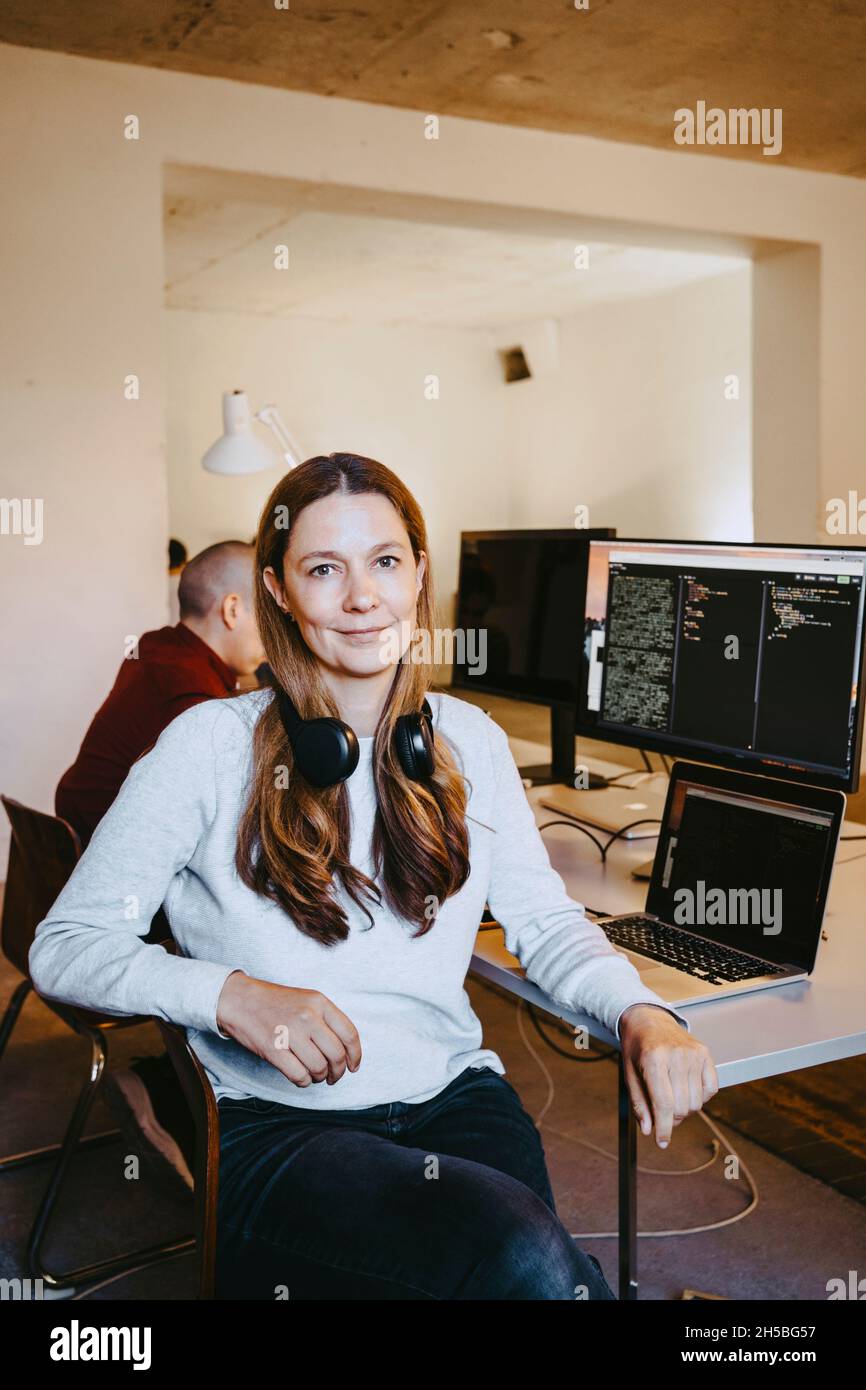 Portrait einer weiblichen Programmiererin mit Laptop und Computer am Schreibtisch im Büro Stockfoto