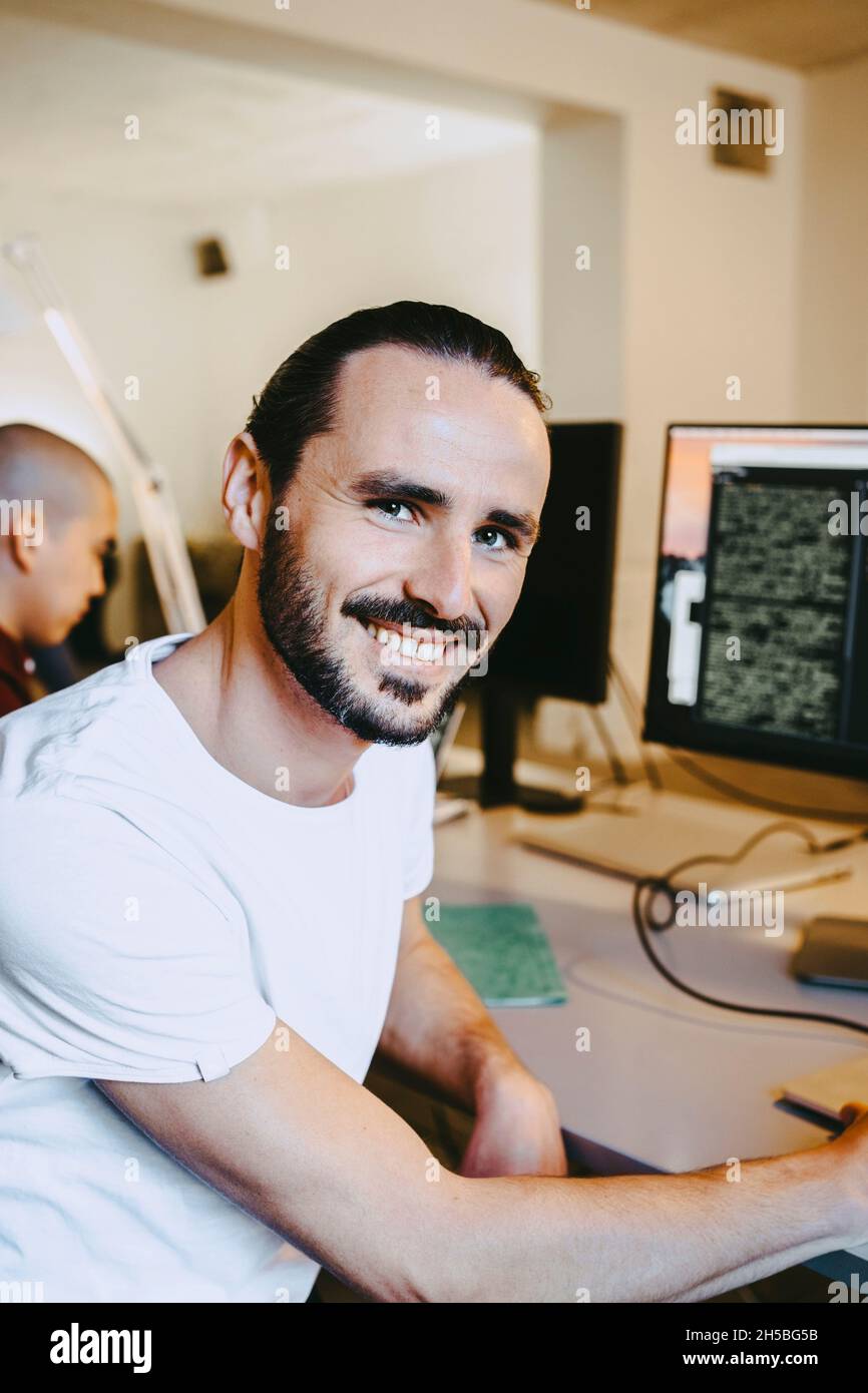 Porträt eines lächelnden männlichen Hackers beim Start in der Schreibtischfirma Stockfoto