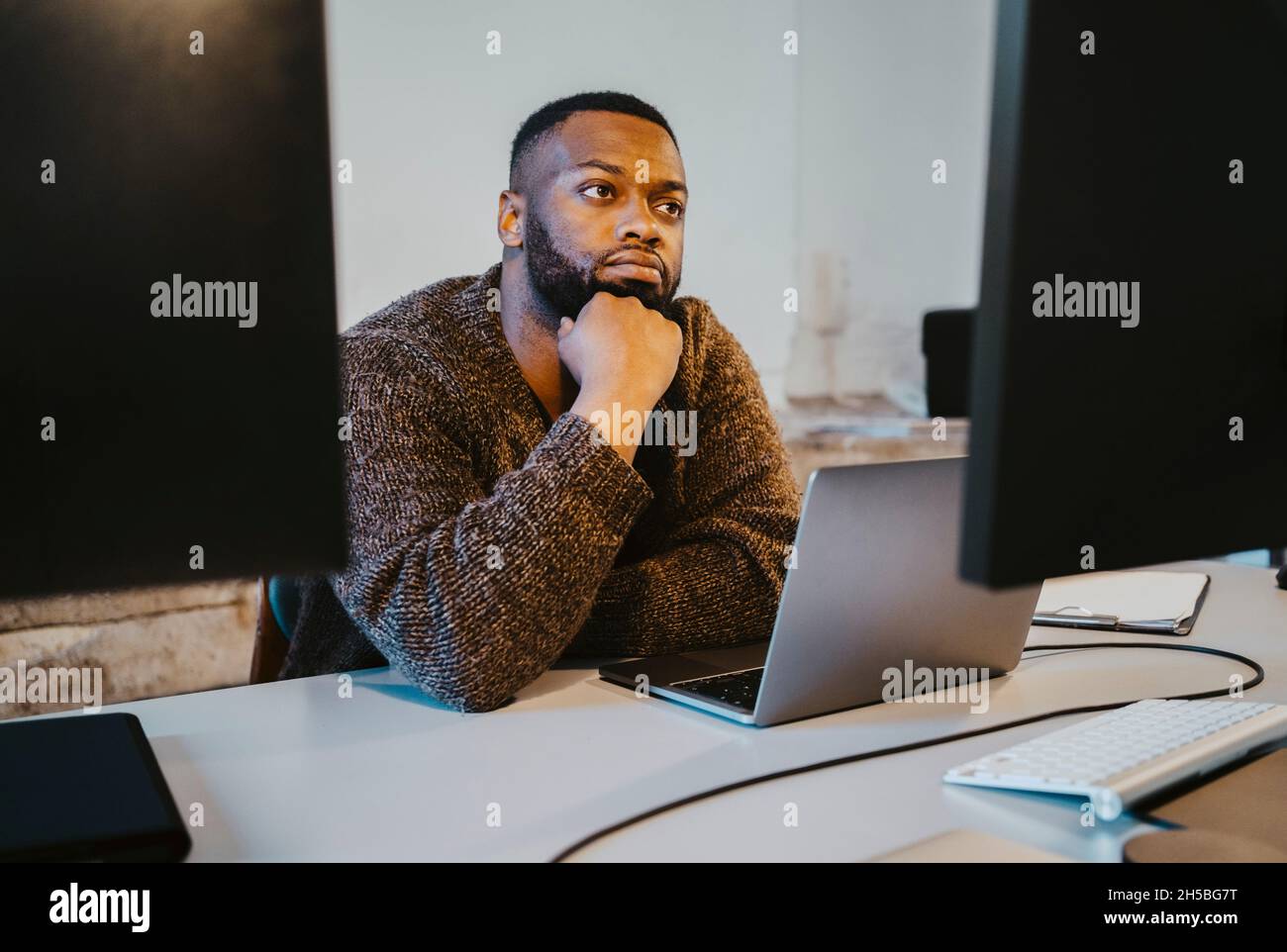 Junger männlicher Hacker mit Laptop, der in einem Startup-Unternehmen nachdenkt Stockfoto