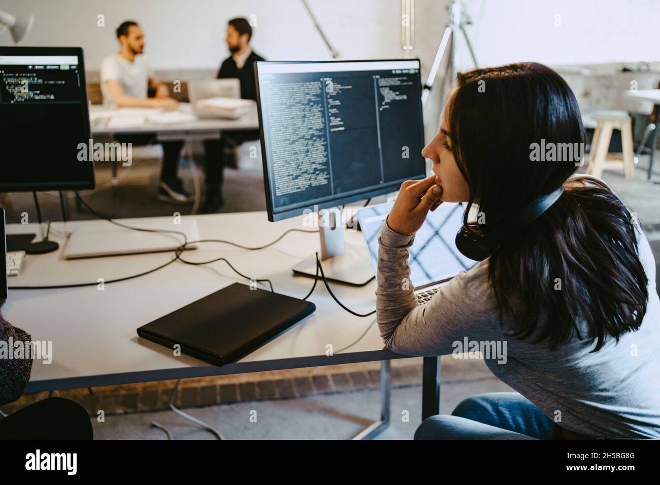 Hackerin, die während ihrer Arbeit in einem Startup-Unternehmen auf den Computer schaut Stockfoto