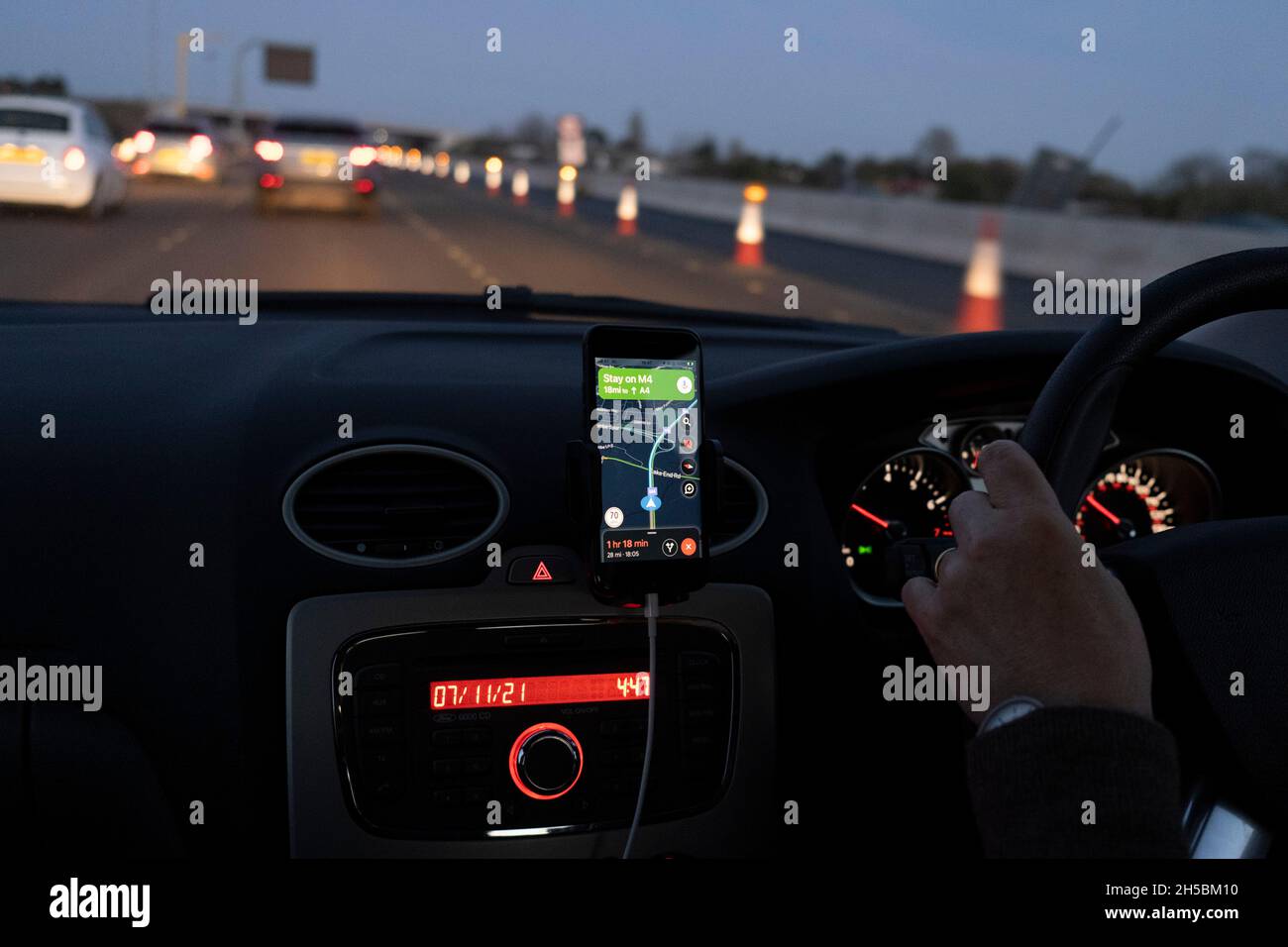 Vom Beifahrersitz eines Autos aus geht am 7. November 2021 in London, England, das Winterlicht durch die Windschutzscheibe in Dunkelheit über, deren Fahrer mit Google Maps auf der Autobahn M4 nach Osten in Richtung London navigiert. Stockfoto