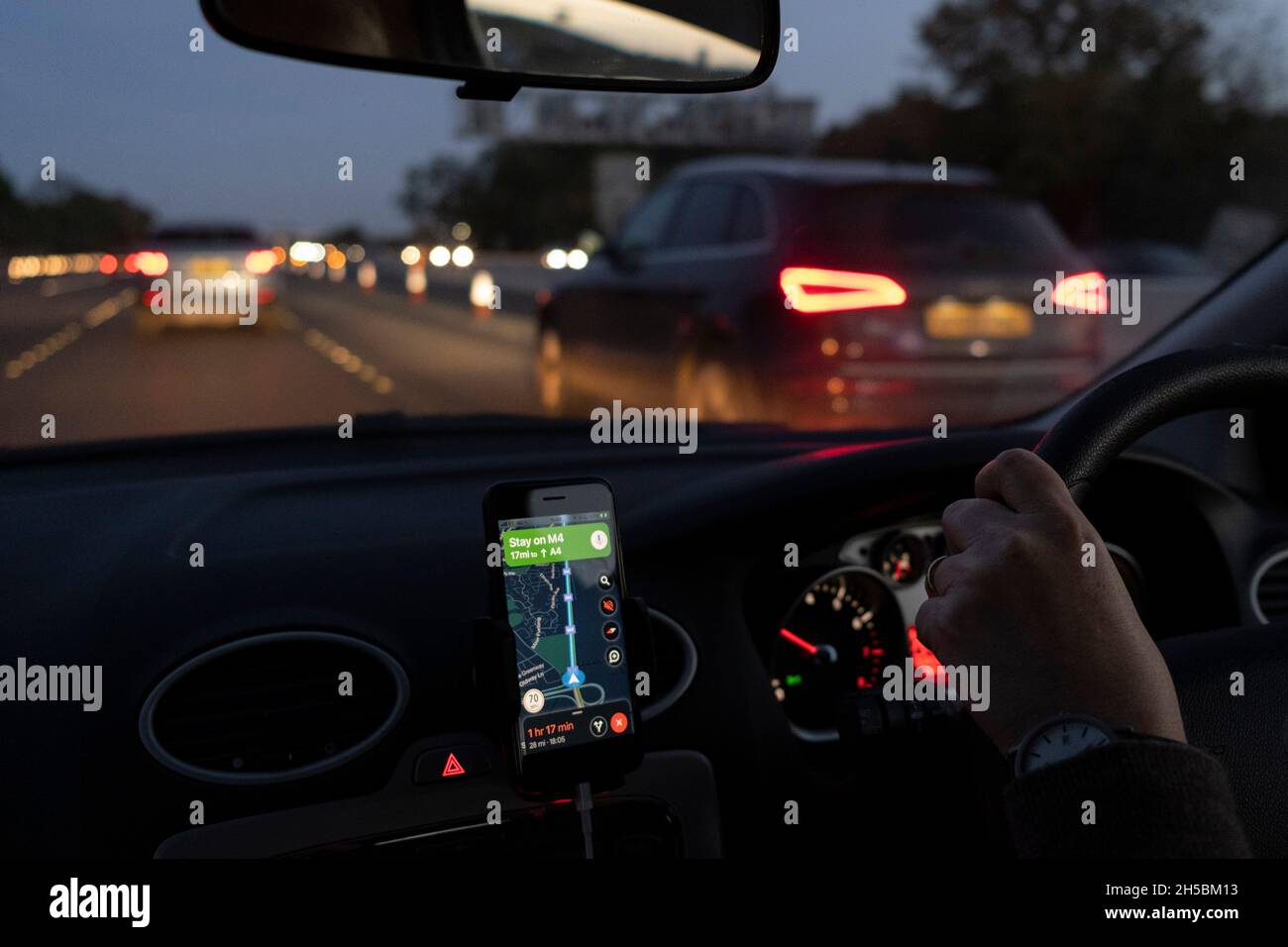 Vom Beifahrersitz eines Autos aus geht am 7. November 2021 in London, England, das Winterlicht durch die Windschutzscheibe in Dunkelheit über, deren Fahrer mit Google Maps auf der Autobahn M4 nach Osten in Richtung London navigiert. Stockfoto