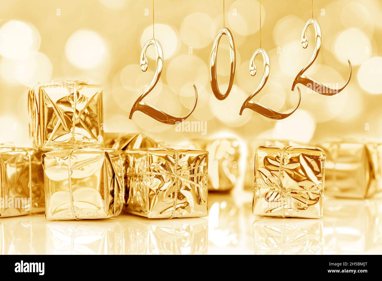 2022, Jahreskarte. Kleine Weihnachtsgeschenke in glänzendem goldenem Papier, Bokeh-Lichter Hintergrund Stockfoto