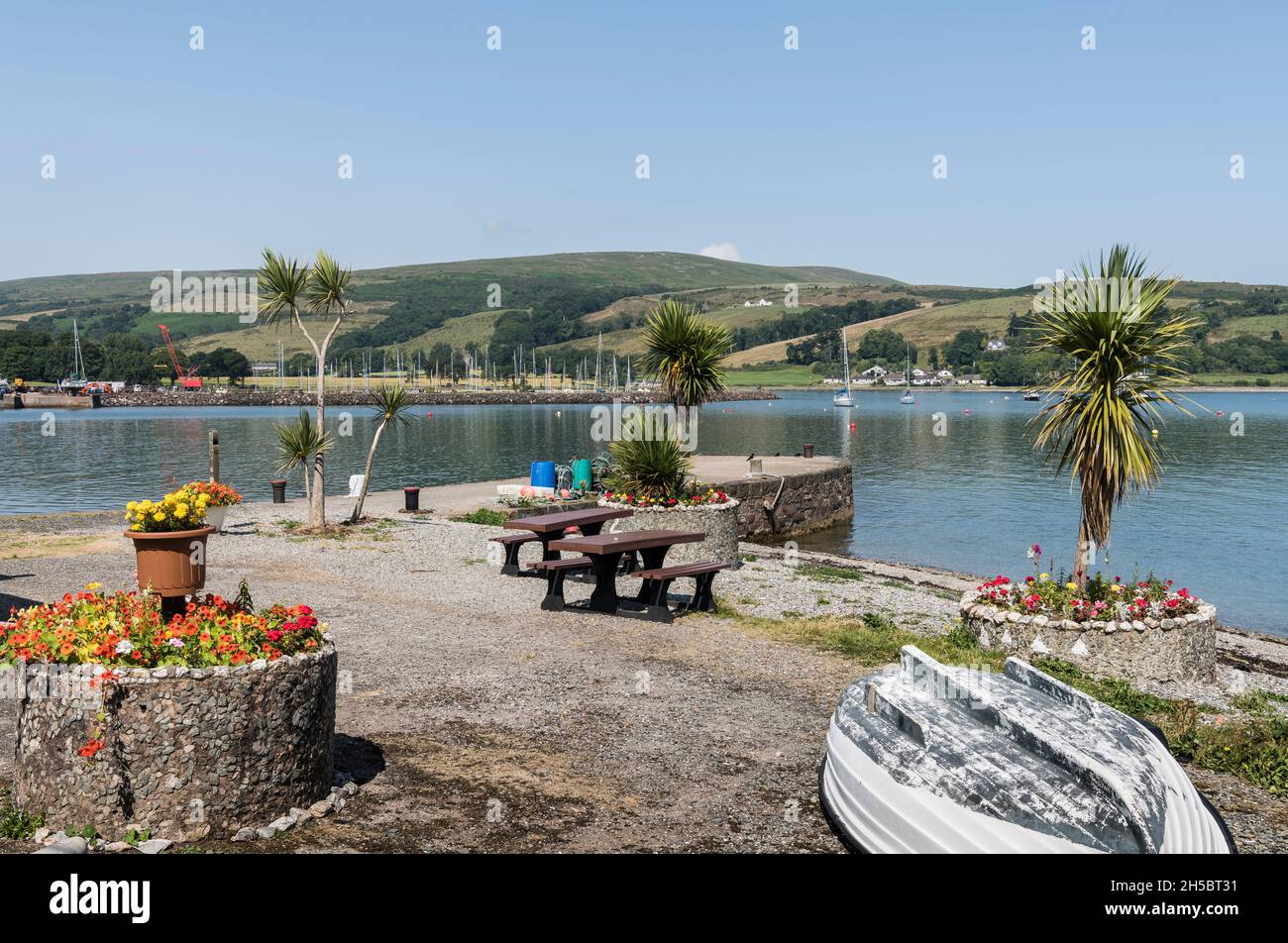 Port Bannatyne Pier und Meeresfront mit Blumen und Palmen, die wie die mediterrane Riviera aussehen, bei strahlendem Sonnenschein mit blauem Himmel, Meer und Yachten. Stockfoto