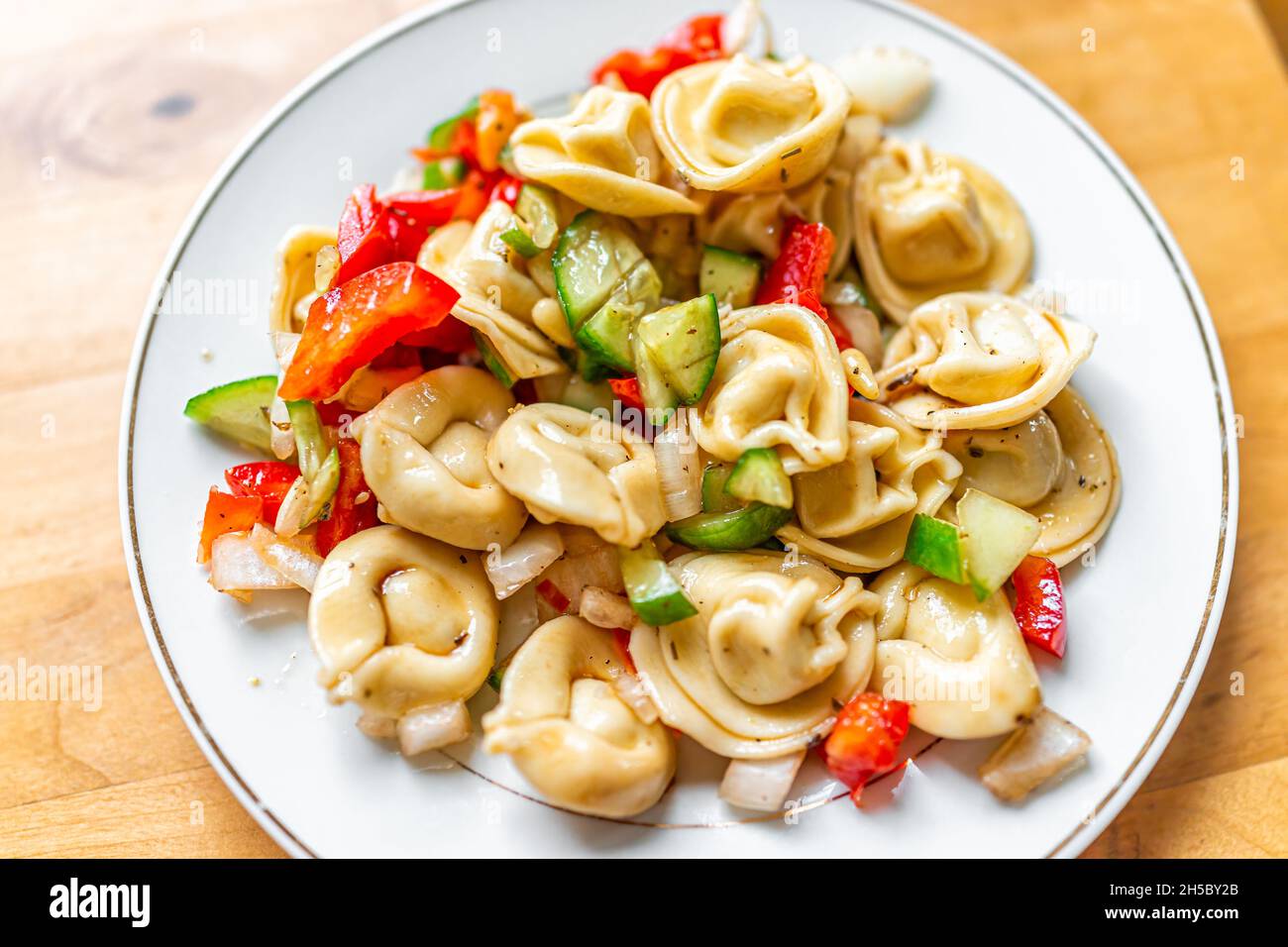 Tortellini-Käse gefüllter Nudelsalat auf der Tabelle oben, flache Ansicht von oben mit geschnittenen Gurken, roten Paprika und Gewürzen auf weißem Teller als gesundes Essen Stockfoto