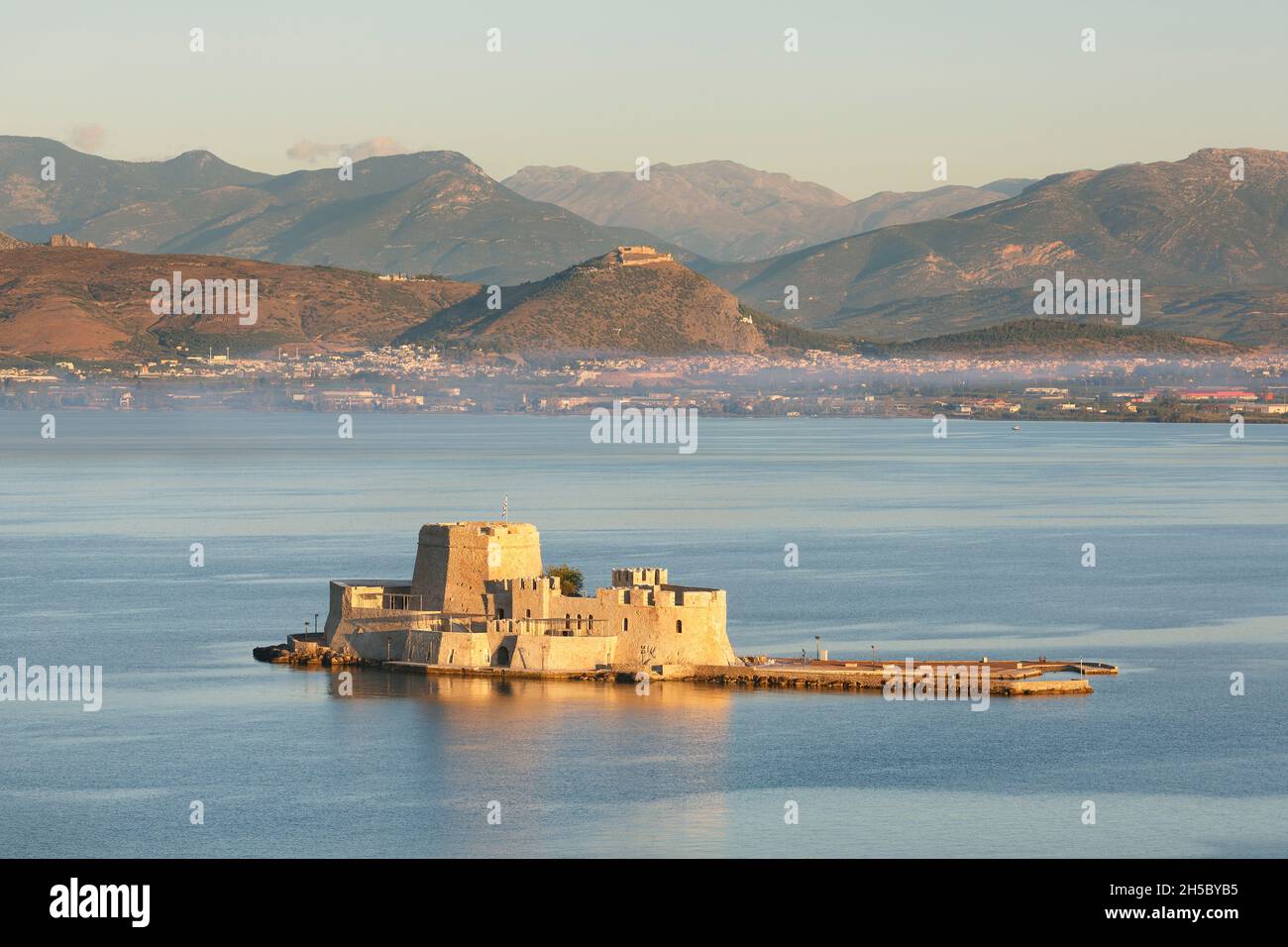 Die Festung von Bourtzi in der Bucht vor der Stadt Nafplio mit der antiken Stätte Argos in der Ferne auf dem Peloponnes von Griechenland Stockfoto