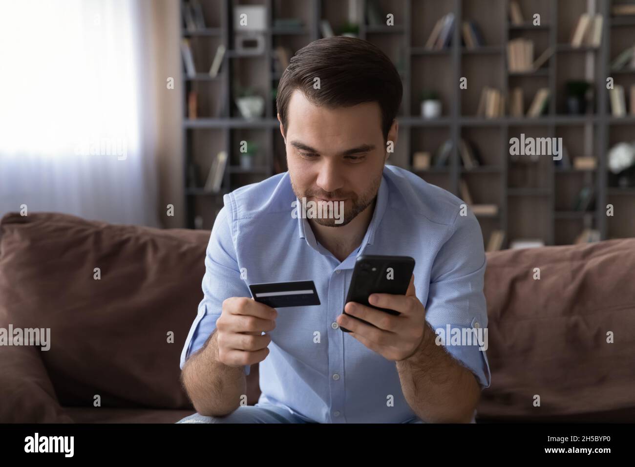 Angenehmer junger Mann, der für Online-Waren oder -Dienstleistungen bezahlt. Stockfoto