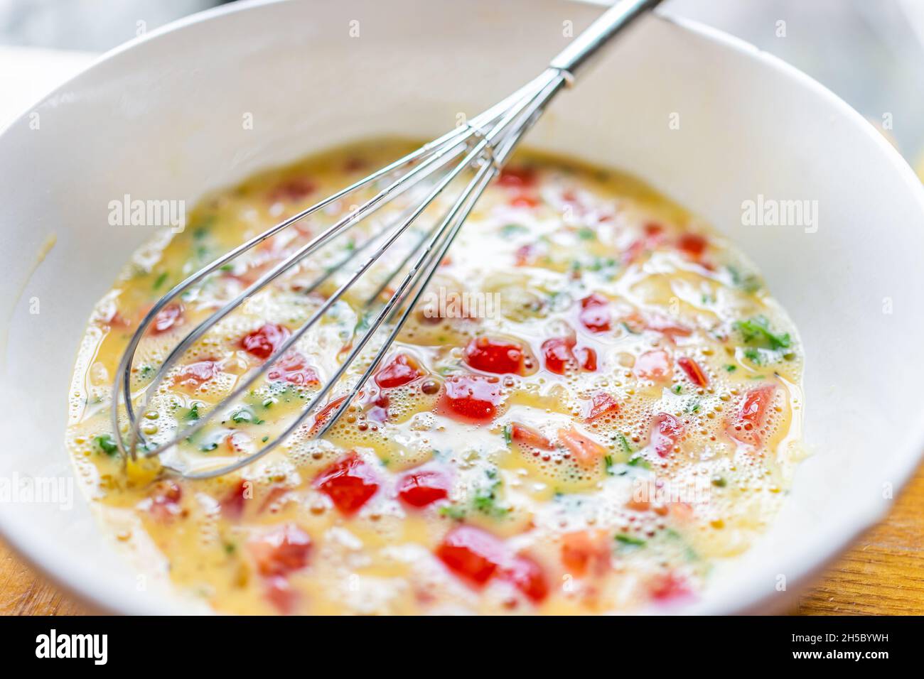 Makro Nahaufnahme der weißen Schüssel Teller mit Ballon Schneebesen Kochen Omelette mit Tomaten, Koriander und roten Paprika Gemüse in der hausgemachten Küche Stockfoto
