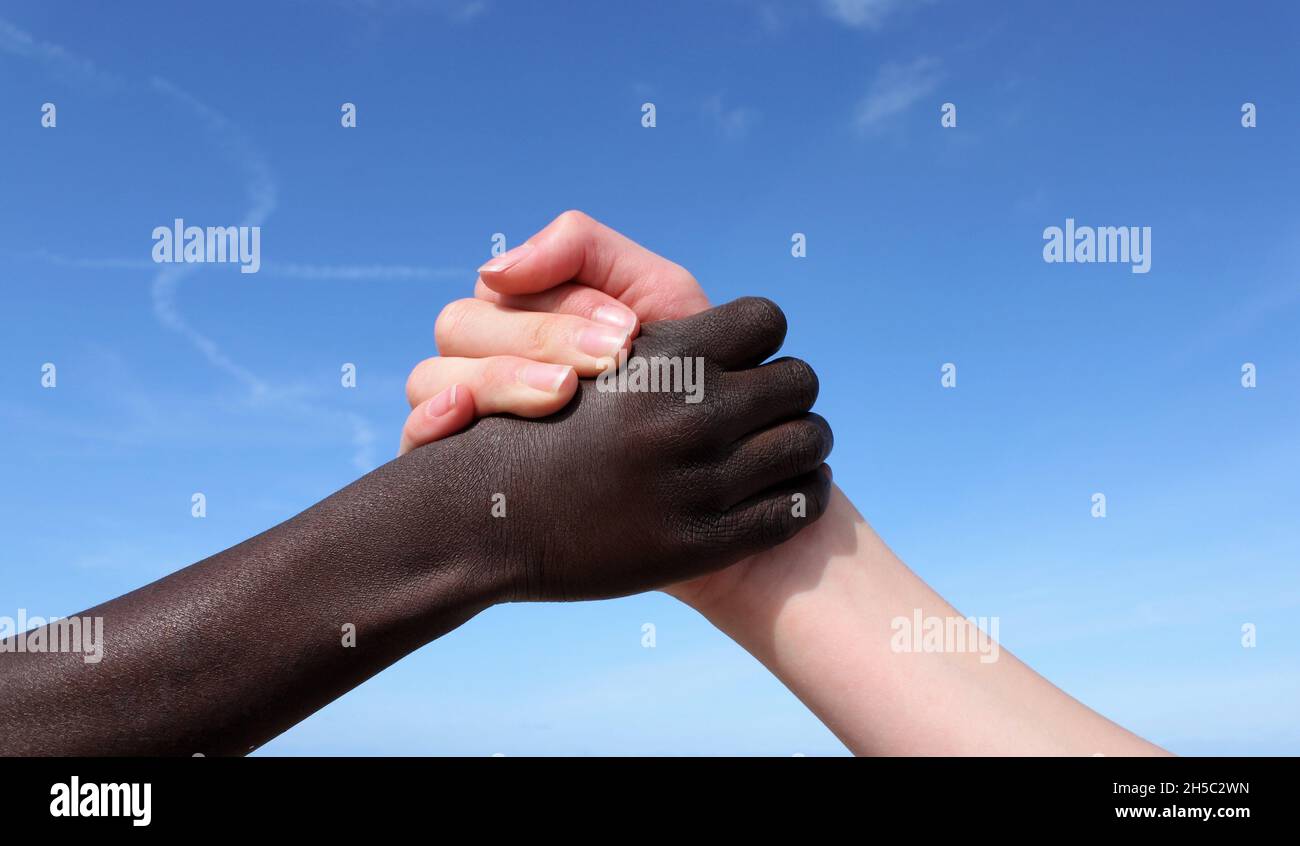Eine weißhäutige Hand und eine schwarzhäutige Hand halten sich gegenseitig vor einem blauen Himmel Stockfoto