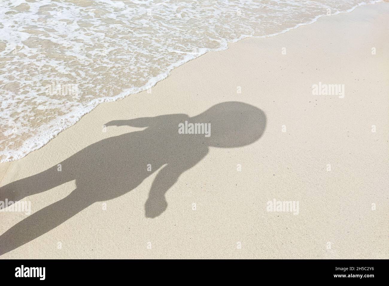 Schatten einer Person mit großem Kopf auf dem Strand Sand mit Meereswellen. Konzept von Aliens, Humanoiden, Unterwasser-Bewohnern Stockfoto