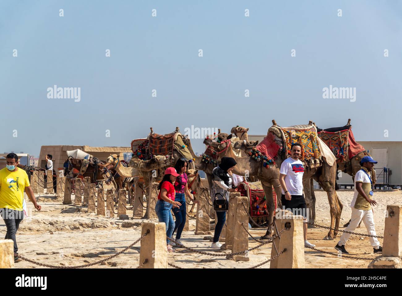 GIZA, ÄGYPTEN - 14. JULI 2021: Eine Gruppe von Menschen und Kamelen in der Nähe der Großen Pyramide in Gizeh, Ägypten Stockfoto