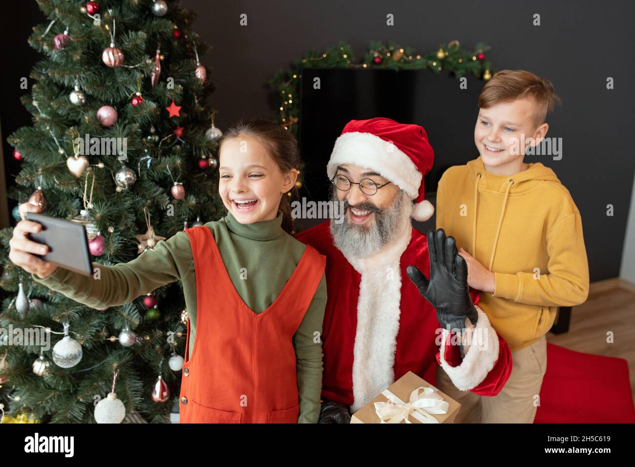 Fröhliche hübsche Mädchen schießen Video mit Weihnachtsmann und Bruder auf dem Smartphone während der Weihnachtszeit zu Hause Stockfoto