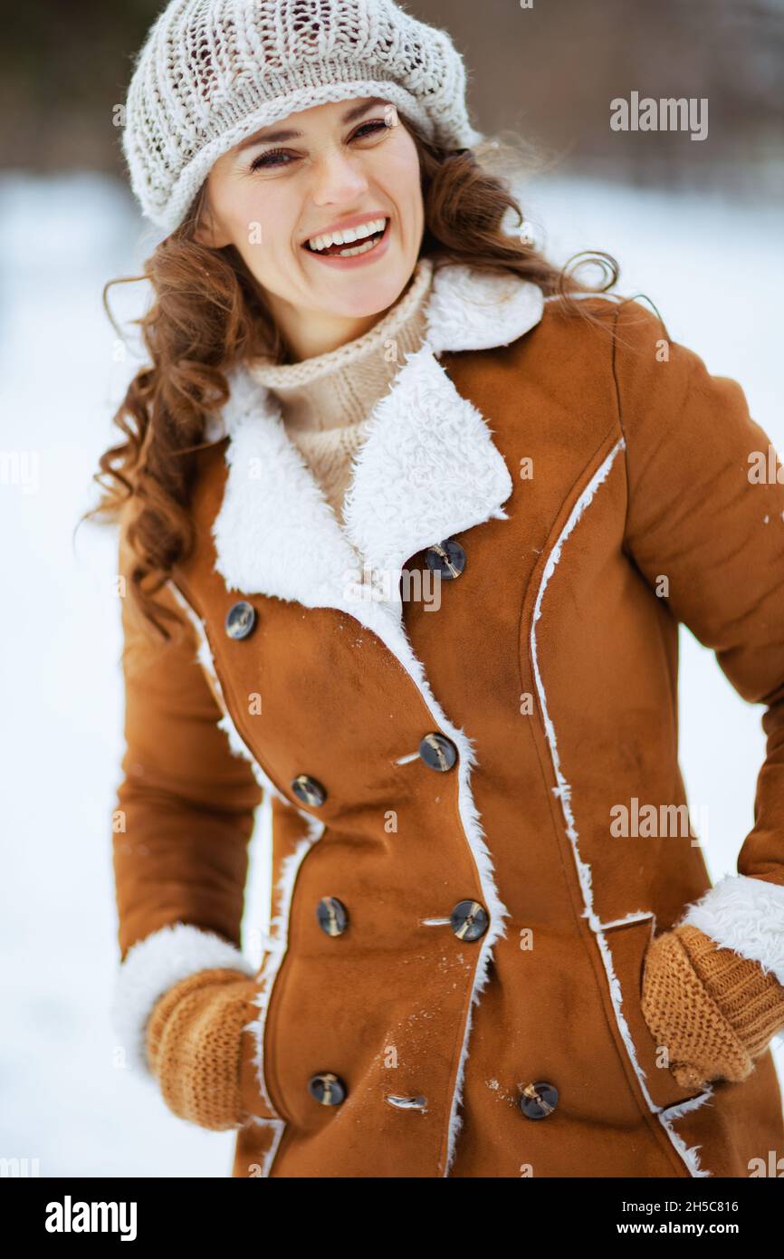Glücklich elegante 40 Jahre alte Frau mit Fäustlingen in einem Strickhut und Schaffell Mantel im Freien im Stadtpark im Winter. Stockfoto