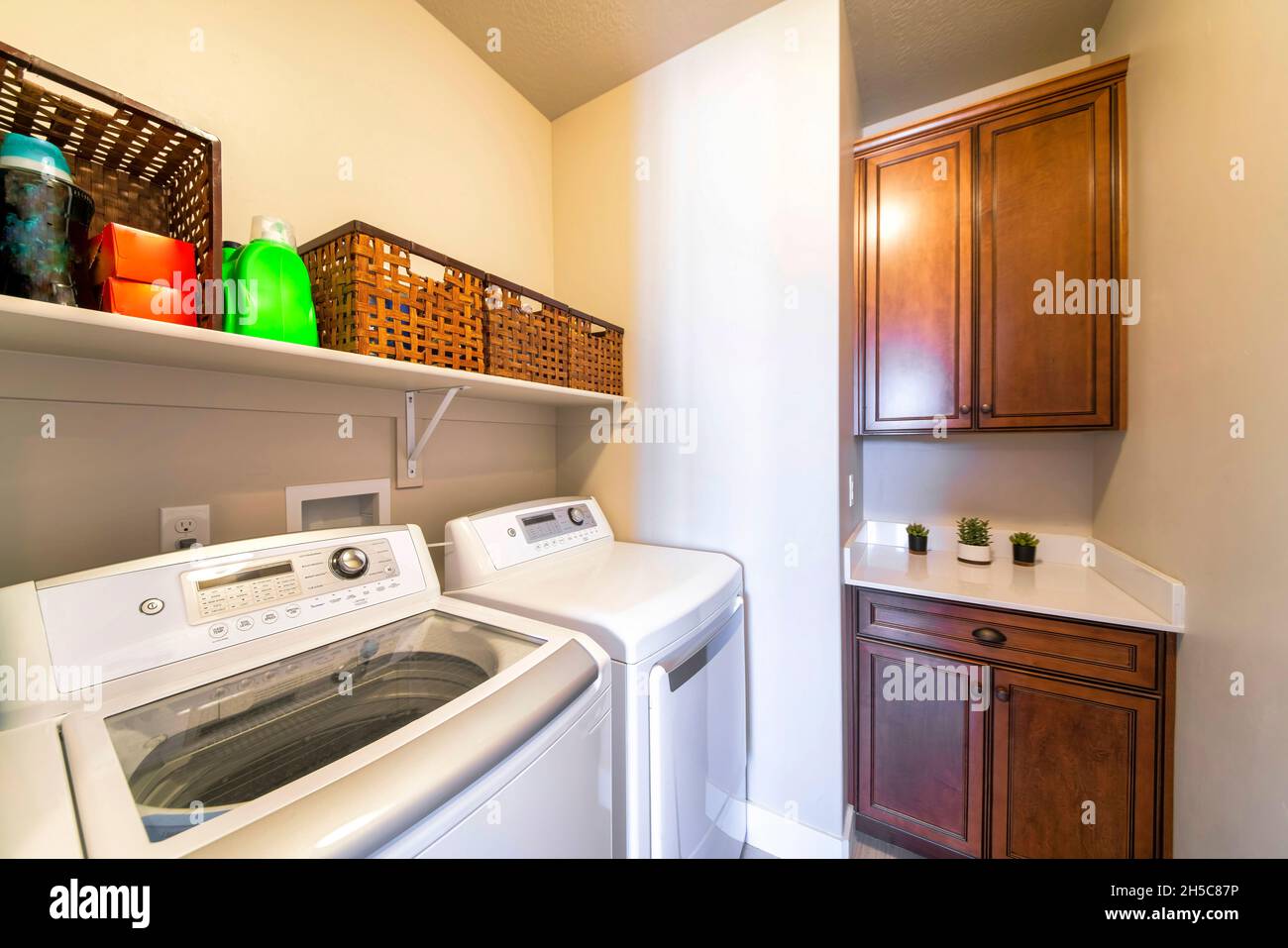 Kleine Waschküche mit Waschmaschinen und Aufbewahrungsschränken aus dunklem Holz Stockfoto