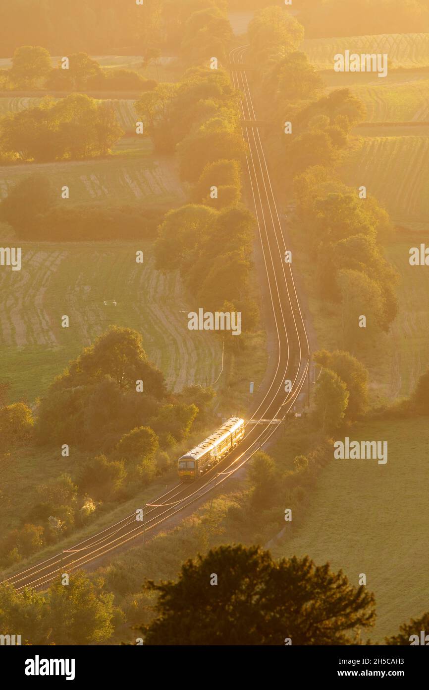 Zug durch englische Landschaft, Surrey, Abendlicht, hoher Aussichtspunkt, North Downs Line. Sonnenlicht, das auf Schienen scheint Stockfoto