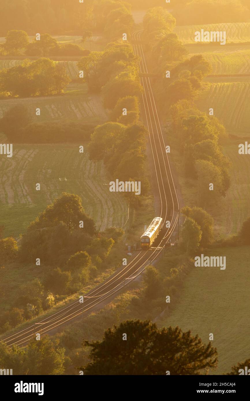 Zug durch englische Landschaft, Surrey, Abendlicht, hoher Aussichtspunkt, North Downs Line. Sonnenlicht, das auf Schienen scheint Stockfoto