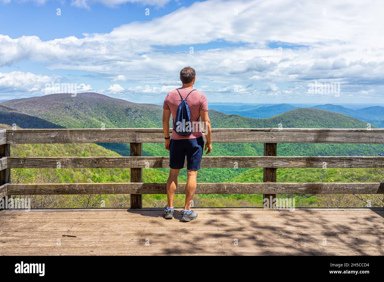 Ein junger Mann mit Rucksack mit Kordelzugbeutel, der auf der Aussichtsplattform steht, überblickt die Holzplattform im Wintergreen-Skiresort in der Natur der Highlands le Stockfoto