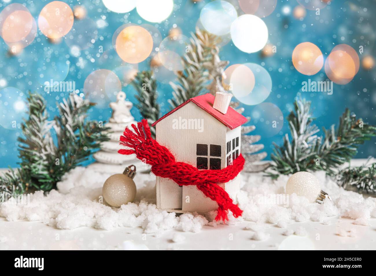 Abstrakter Advent Weihnachten Hintergrund. Spielzeughaus mit gestricktem Schal und Winterdekorationen auf blauem Hintergrund mit Schnee und entkockter Girlande Stockfoto