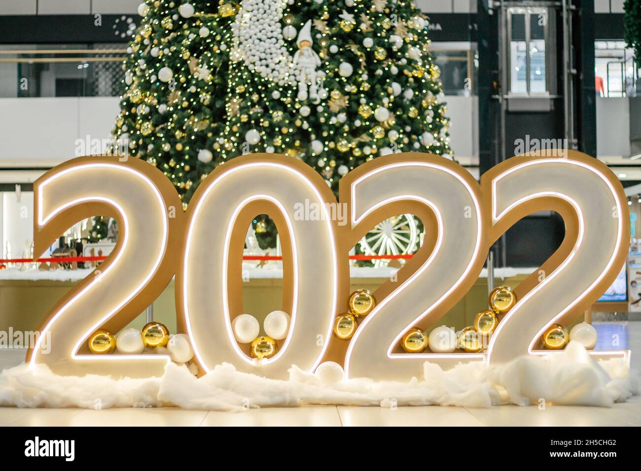Große, leuchtende Zahlen 2022 in der Halle auf dem Boden vor dem Hintergrund eines geschmückten Weihnachtsbaums. Frohe Weihnachten und ein glückliches neues Jahr 2022 Stockfoto