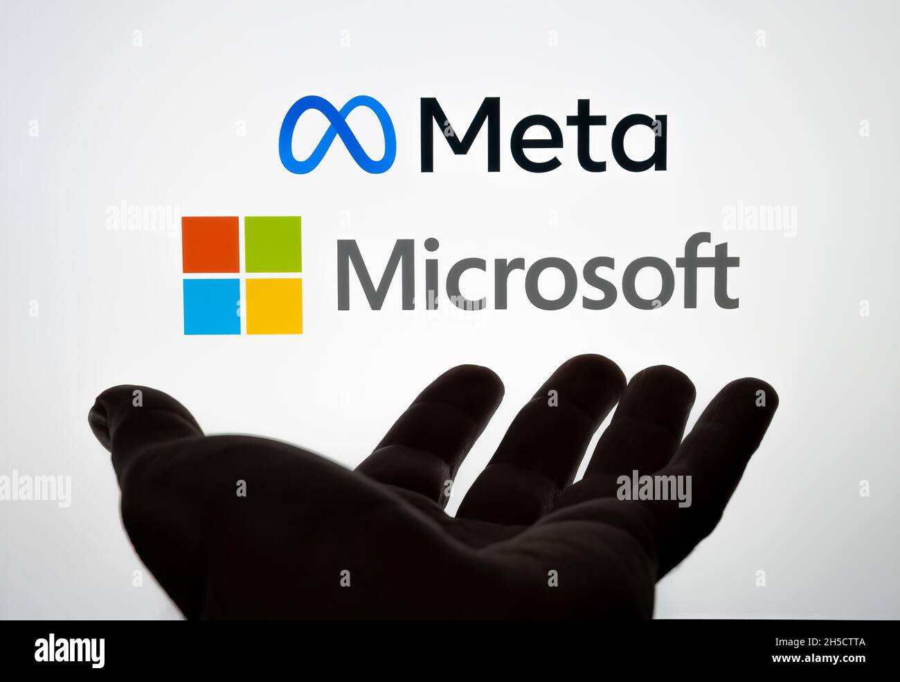 Silhouette der Hand vor und verschwommen FACEBOOK META und MICROSOFT Firmenlogos auf Laptop-Bildschirm hinter gesehen. Selektiver Fokus. Stafford, United King Stockfoto