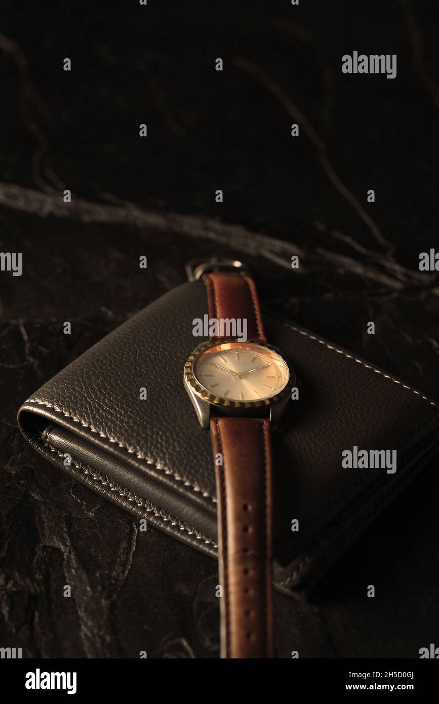 Uhr und Brieftasche auf dunklem Schieferhintergrund, seitlich beleuchtet mit warmen Tönen und Kopierraum. Stockfoto