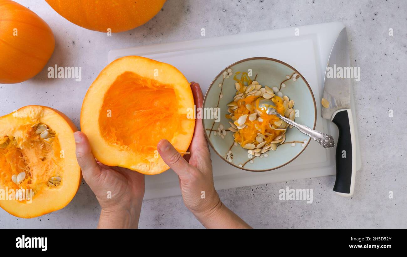 Frau schaufelt weiches Fleisch und Samen aus der Mitte des Kürbisses, flach liegend, grauer Steinhintergrund Stockfoto