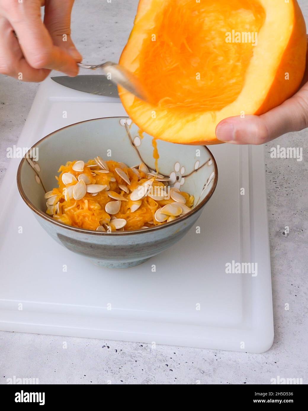 Frau schaufelt weiches Fleisch und Samen aus der Mitte des Kürbisses, flach liegend, grauer Steinhintergrund Stockfoto