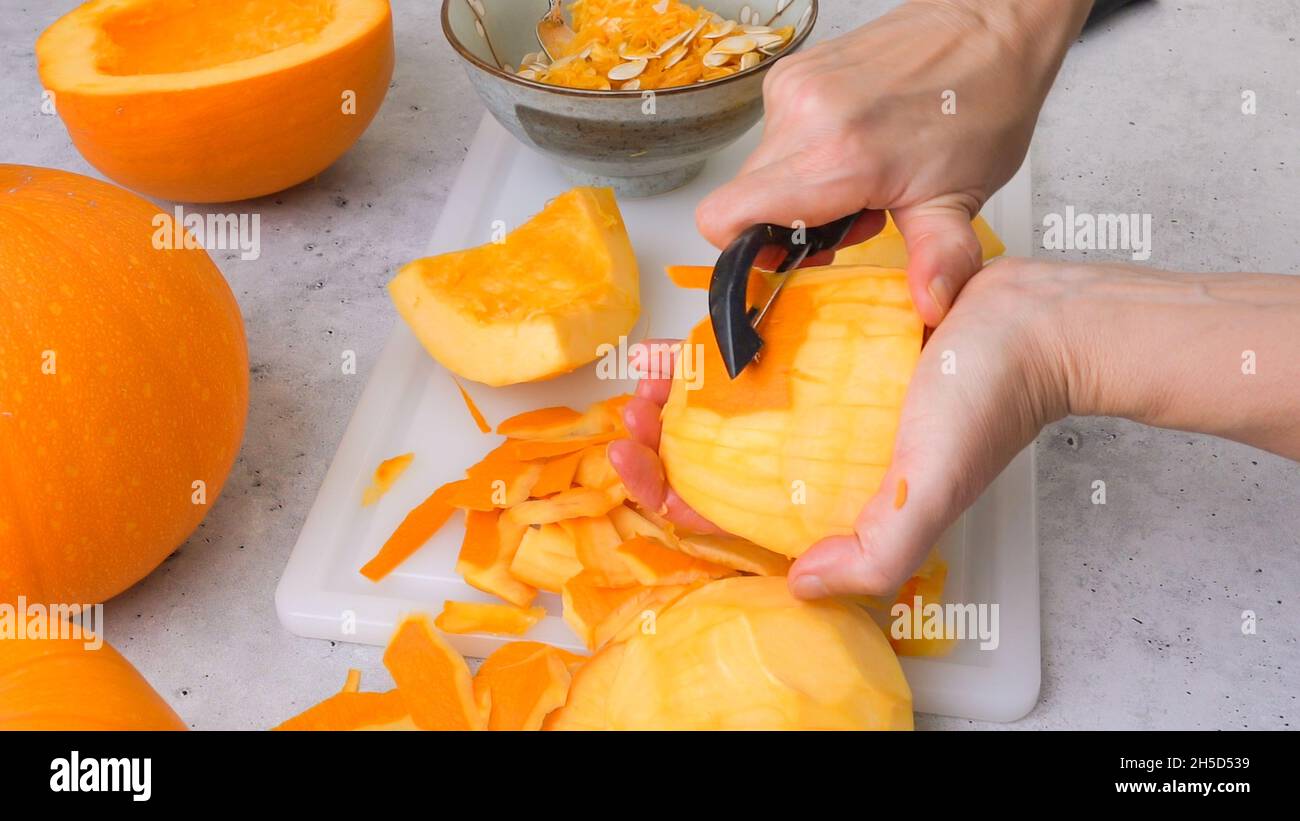 Frau Hände schälen frischen rohen orangen Kürbis, Nahaufnahme auf grauem Stein Hintergrund Stockfoto