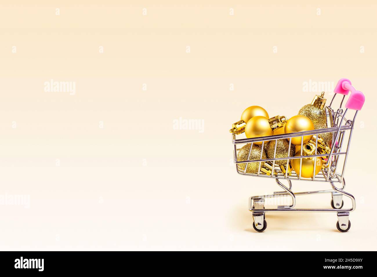 Trolley-Einkaufswagen mit goldenen Weihnachtskugeln auf hellem Hintergrund mit Kopierfläche. Weihnachtsangebote, Rabatte, Weihnachtseinkäufe und Geschenke kaufen und Pre Stockfoto