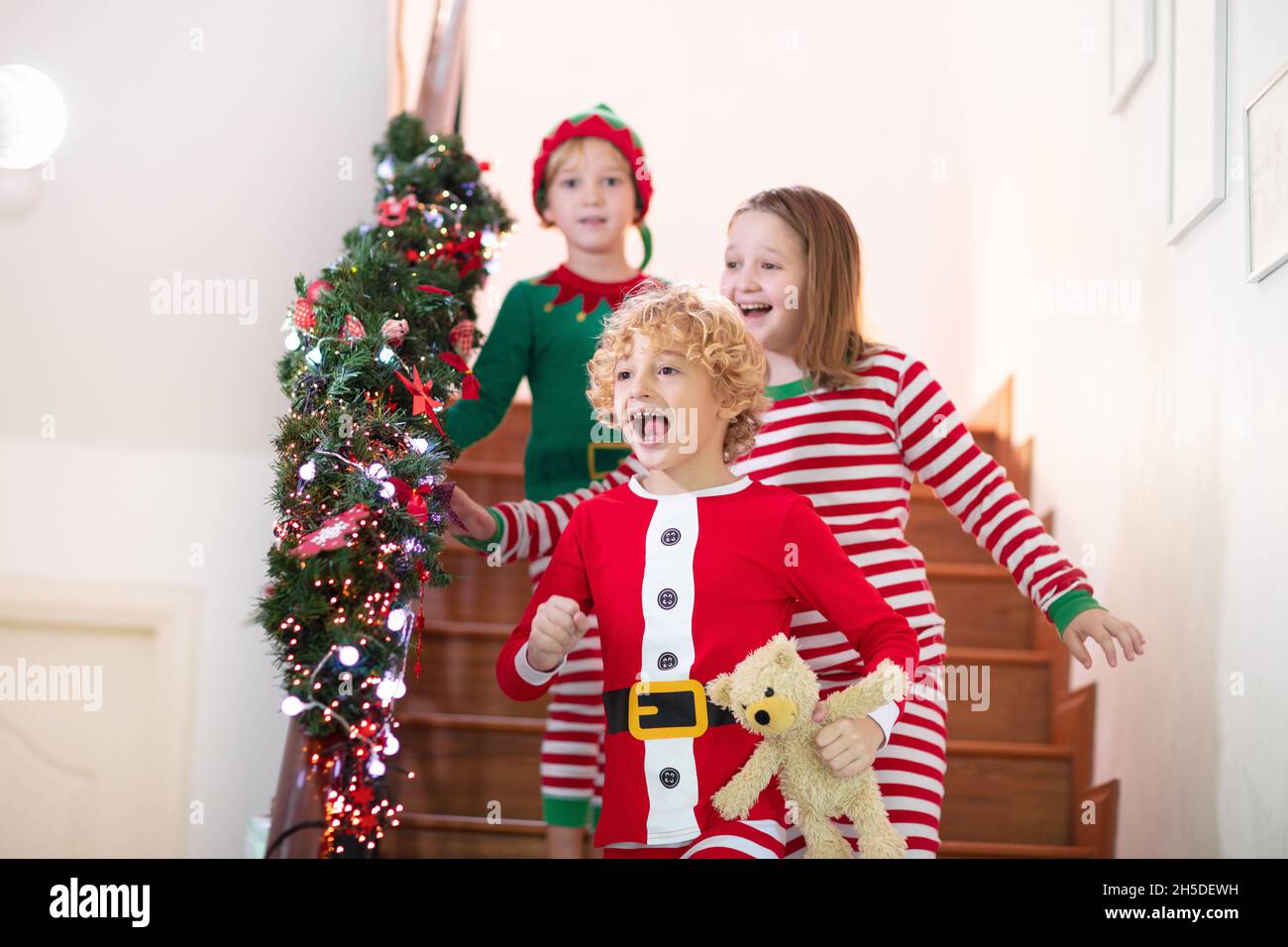 Kinder laufen Treppen am Weihnachtsmorgen. Kinder im Schlafanzug laufen nach unten, um Weihnachtsgeschenke zu öffnen. Feiern zu Hause. Familienurlaub im Winter. Stockfoto