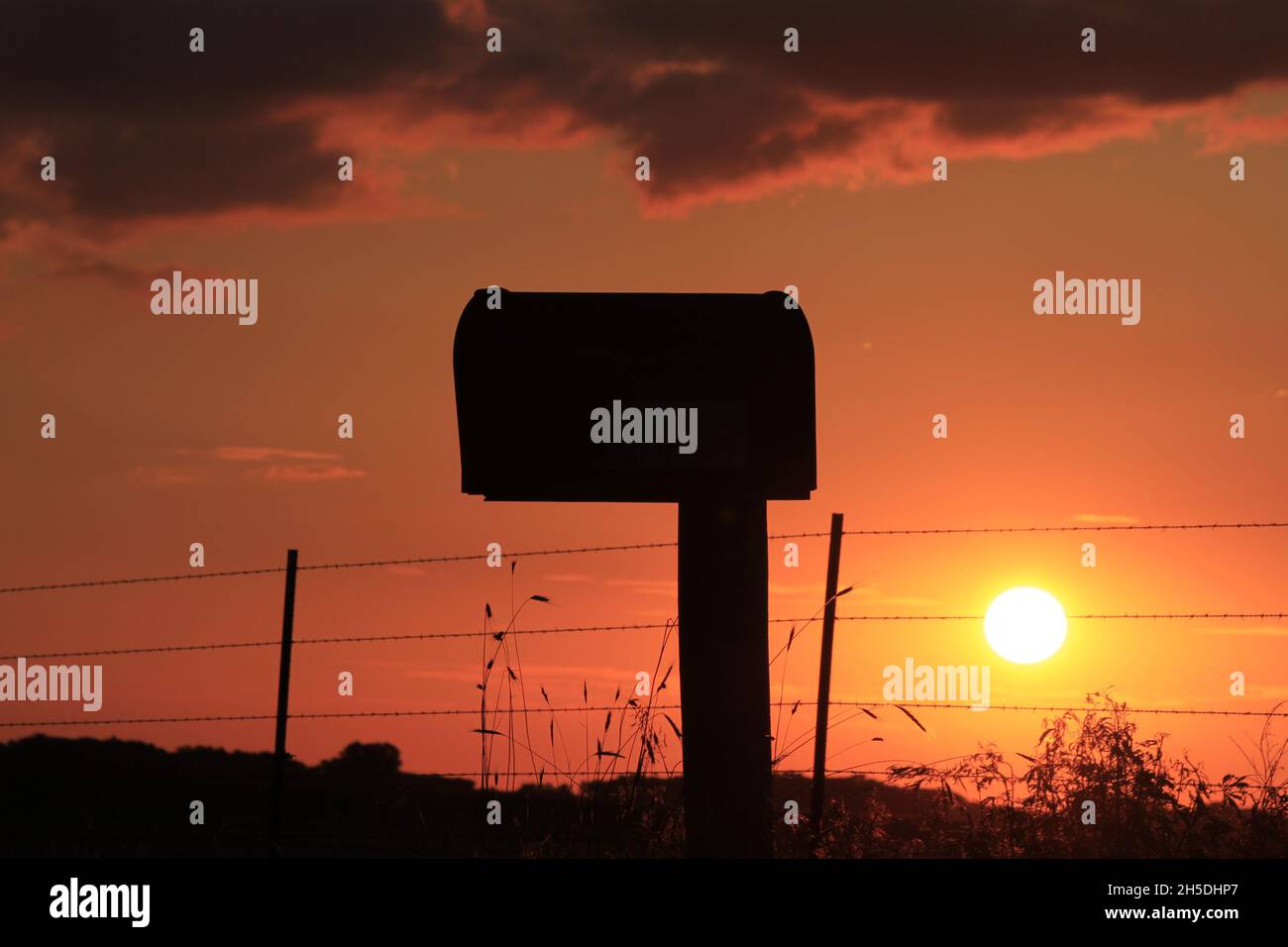 Kansas bunte Blazing orange Sonnenuntergang mit einem Briefkasten Silhouette auf dem Land. Stockfoto