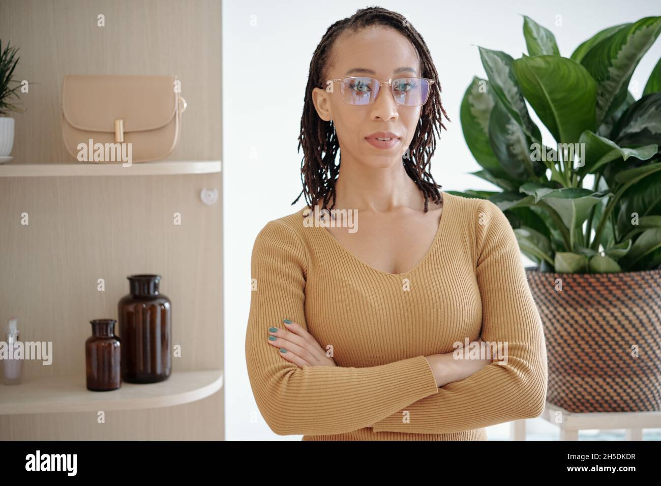 Schöne selbstbewusste schwarze Frau in Brille und Kamelpullover über die Arme und Blick auf die Kamera Stockfoto