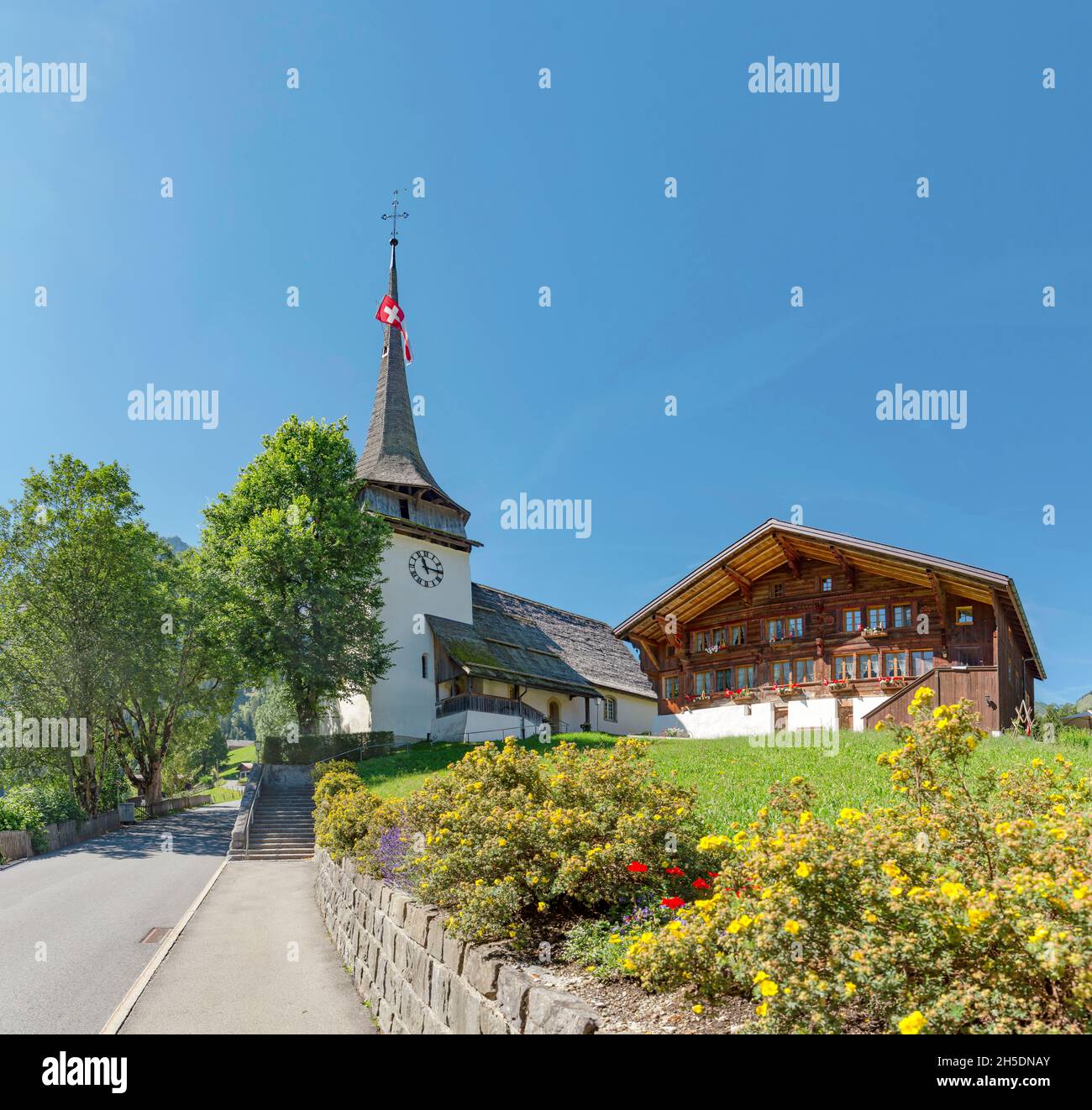 Chalet und Kirche *** Ortsüberschrift *** Gsteig bei Gstaad, Kanton Bern, Schweiz, Stadt, Dorf, Blumen, Sommer, Berge, Hügel, Stockfoto